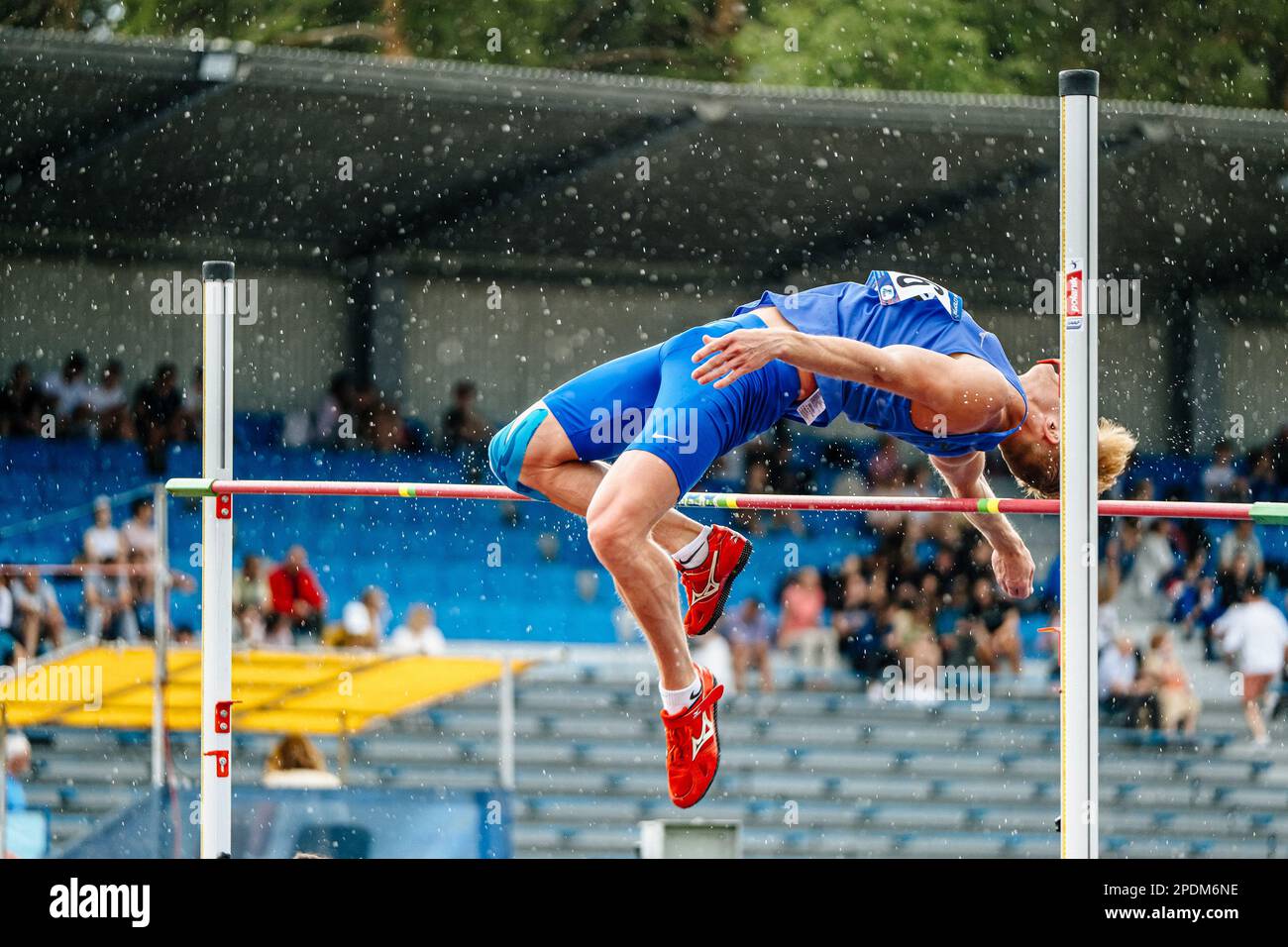 Männlicher Athlet-Pullover mit hohem Sprung im Regen, Sportwettkampf, Mizuno Spikes Schuhe zum Springen, Sportfotos Stockfoto