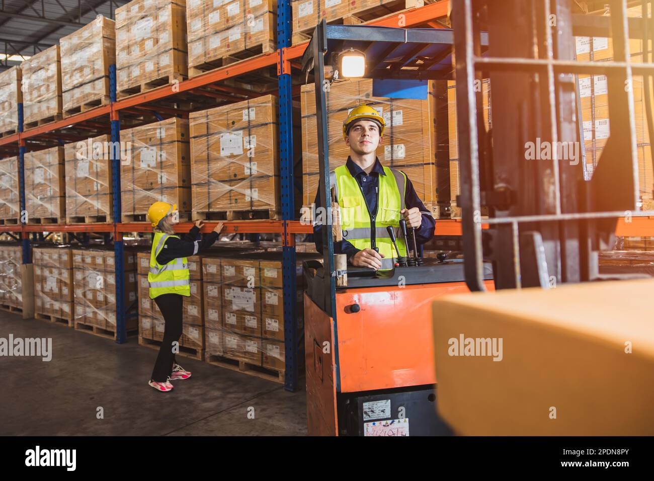 Weißer Mann, der im Warenlager arbeitet. Lagermitarbeiter, die die Produkte mit Palettenhubwagen transportieren. Stockfoto