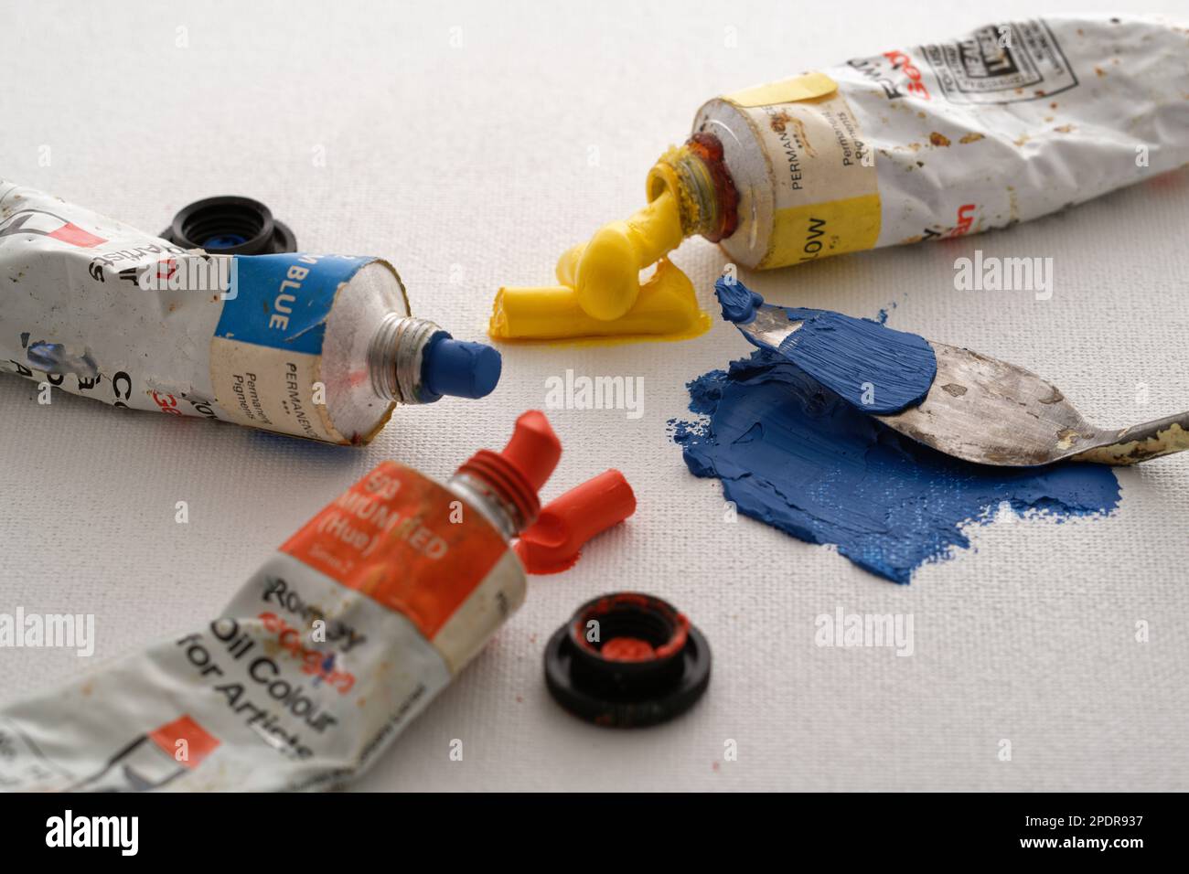 Farbige Ölfarben und ein Palettenmesser auf einem Hintergrund aus Leinwand. Blau, Rot und Gelb, um ein Bild zu machen. Der kreative Prozess. Stockfoto