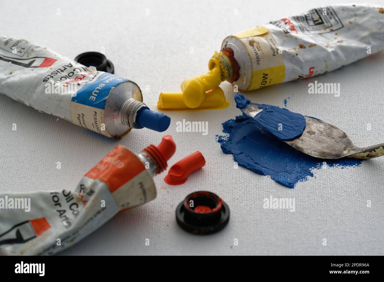 Farbige Ölfarben und ein Palettenmesser auf einem Hintergrund aus Leinwand. Blau, Rot und Gelb, um ein Bild zu machen. Der kreative Prozess. Stockfoto