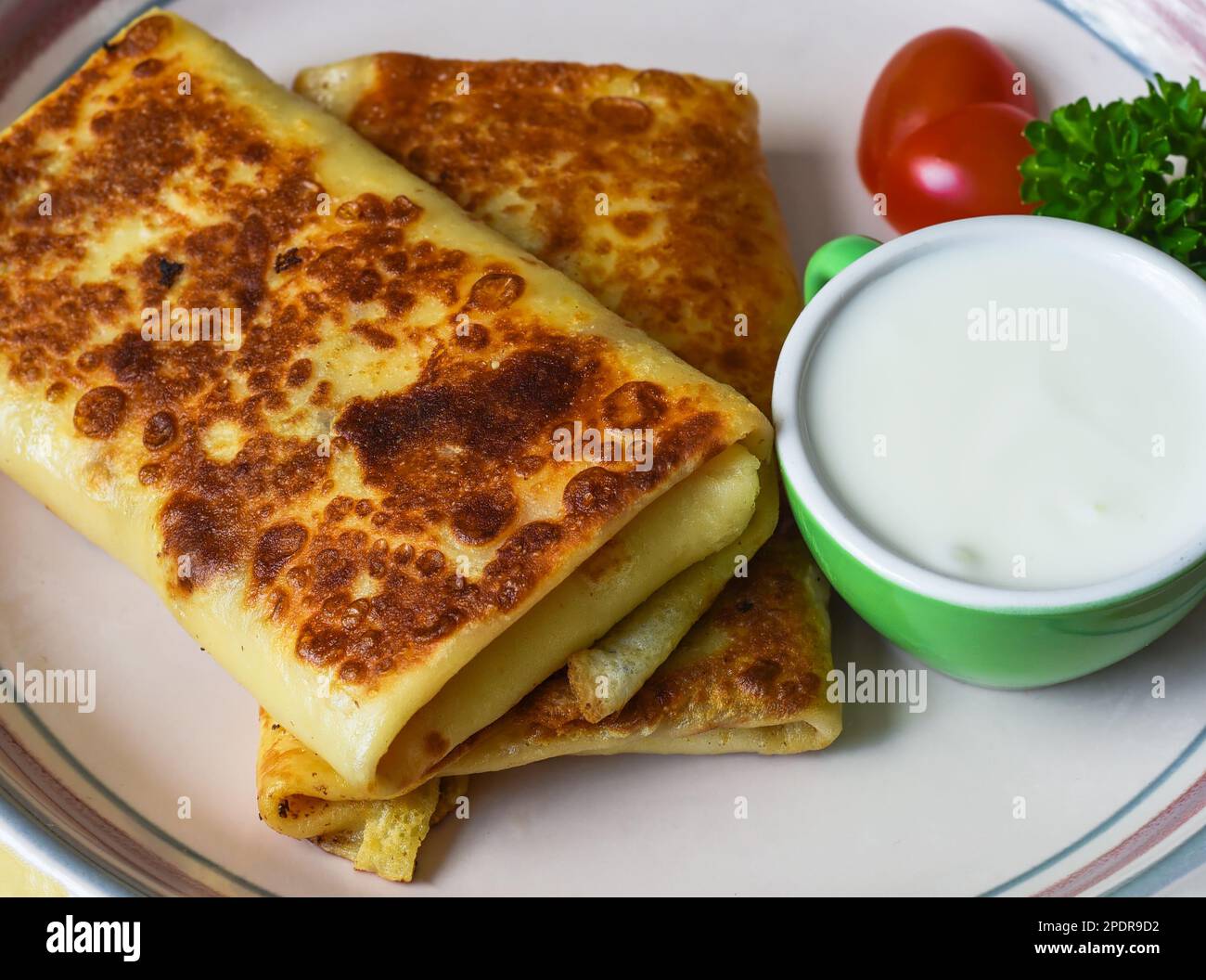 Gefaltete gefüllte Pfannkuchen mit Sahne-Sauce auf weißem Teller Stockfoto