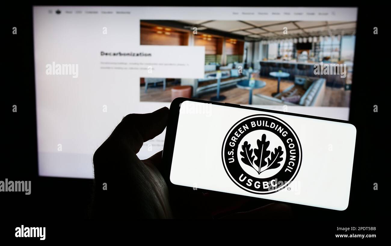 Person, die ein Mobiltelefon mit dem Logo des US Green Building Council (USGBC) auf dem Bildschirm vor der Webseite hält. Konzentrieren Sie sich auf das Display des Telefons. Stockfoto