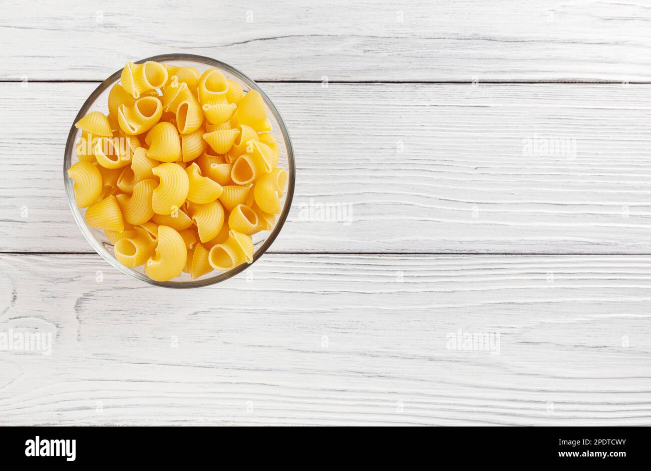 Ungekochte Pfeifenspachtelpasta in Glasschüssel auf weißem Holzhintergrund mit Kopierbereich Stockfoto