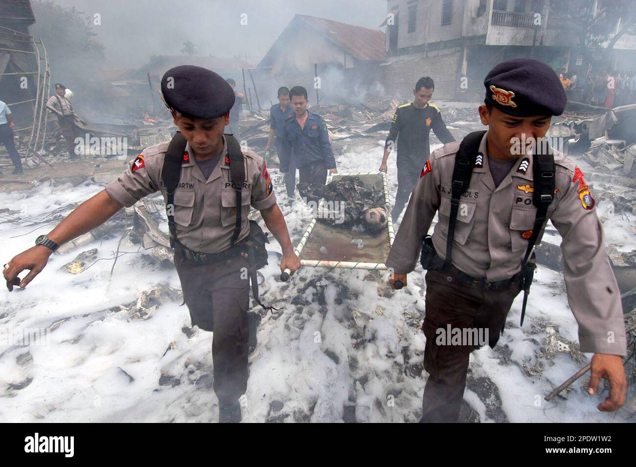 ** EDITORS NOTE: GRAPHIC CONTENT ** Indonesian police officers carry the body of a victim killed in a crash of a Mandala Airlines Boeing 737-200 jetliner in Medan, North Sumatra, Indonesia, Monday, Sept. 5, 2005. The Indonesian jetliner crashed into a crowded residential neighborhood in the city of Medan shortly after takeoff Monday, killing 111 people on board and an unknown number on the ground, officials said. (AP Photo/Yuli) Stockfoto