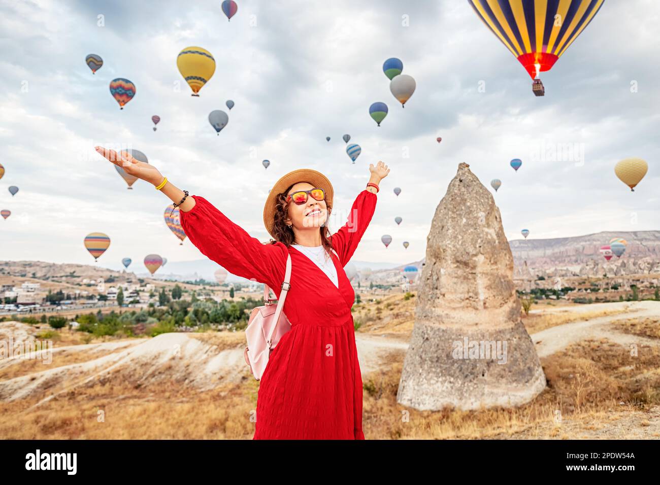 Ein Mädchen in einem Kleid, das sich in den atemberaubenden Anblick fliegender Heißluftballons in Kappadokien, dem Paradies für Reisende, eingefangen hat. Stockfoto