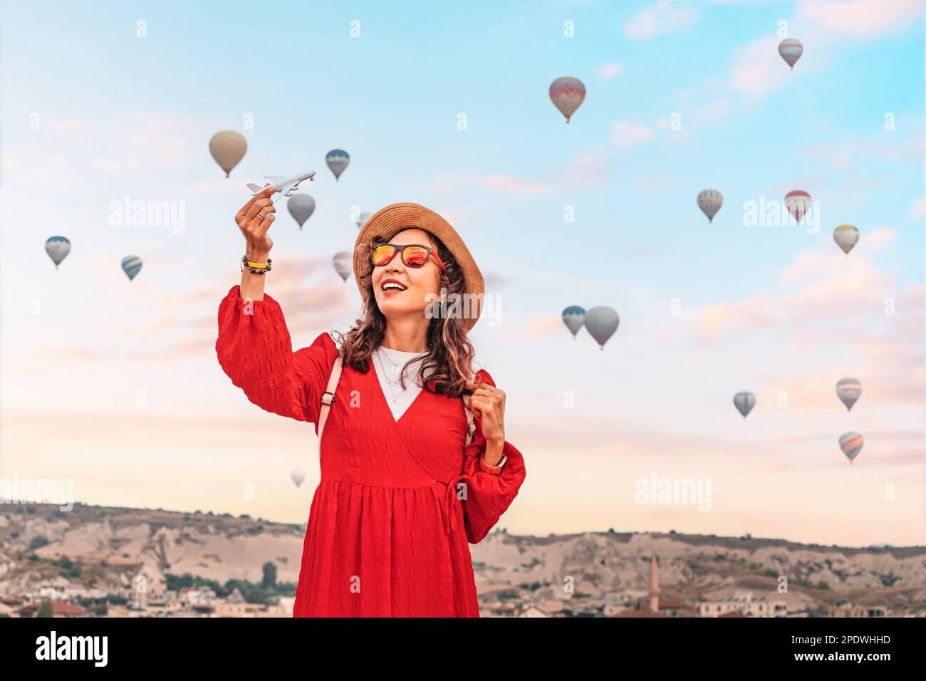 Das Mädchen hält ein Spielzeugflugzeug mit Kappadokiens Heißluftballons im Hintergrund und repräsentiert das Flugzeugtransport- und Reisekonzept. Stockfoto