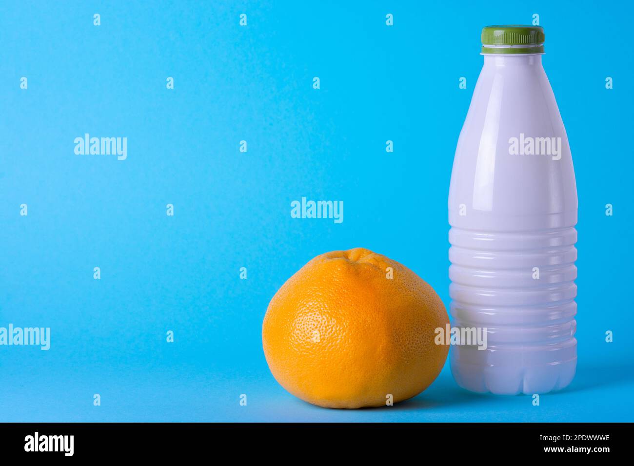 Weiße Kunststoffflasche auf hellblauem Hintergrund mit Grapefruit. Gesunde Ernährung. Milchprodukte. Frisches Obst Stockfoto