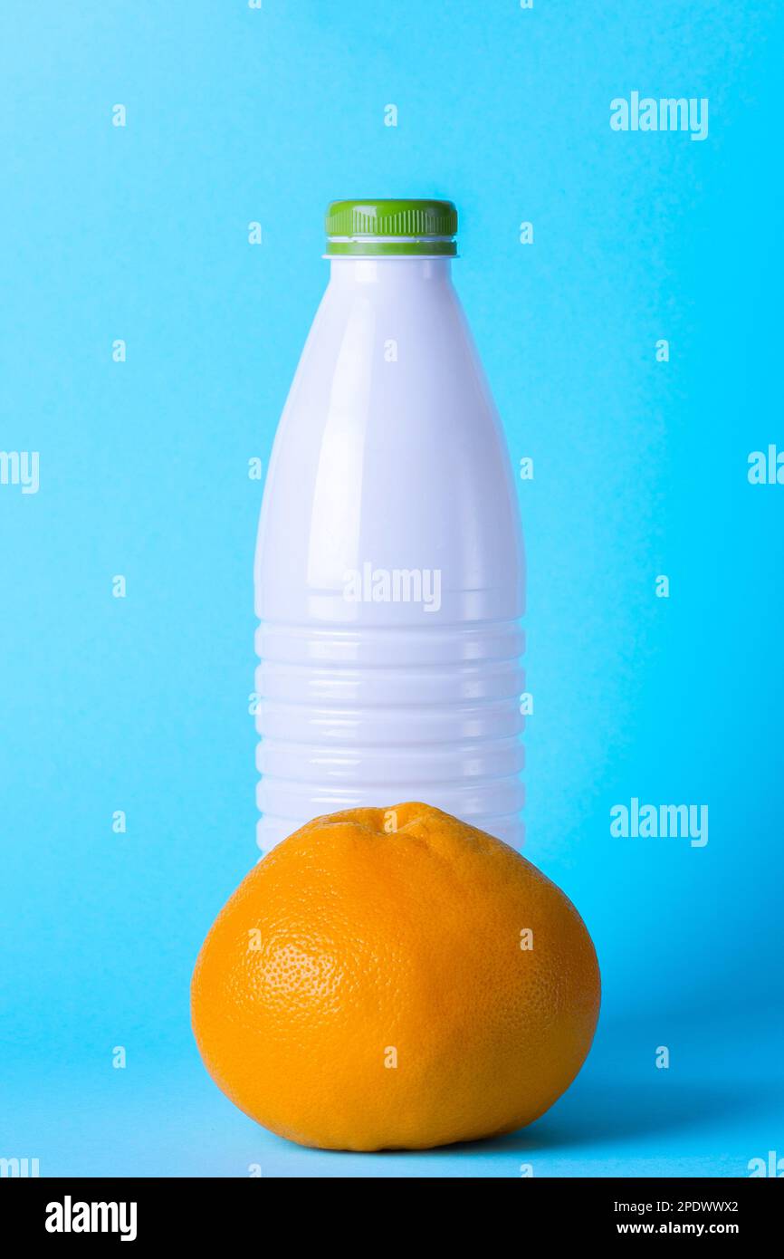Weiße Kunststoffflasche auf hellblauem Hintergrund mit Grapefruit. Gesunde Ernährung. Milchprodukte. Frisches Obst Stockfoto