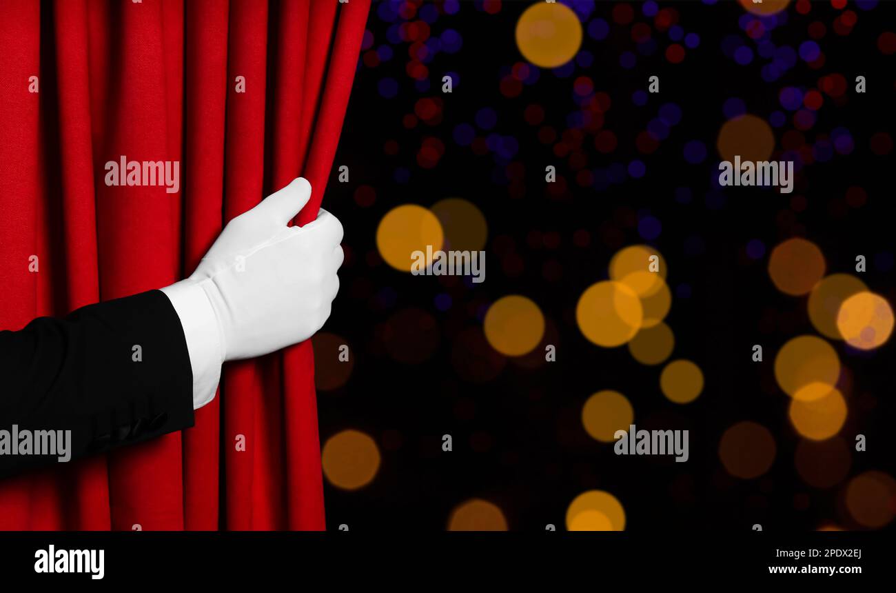 Mann öffnet roten Vorhang vor unscharfen Lichtern. Bokeh-Effekt Stockfoto