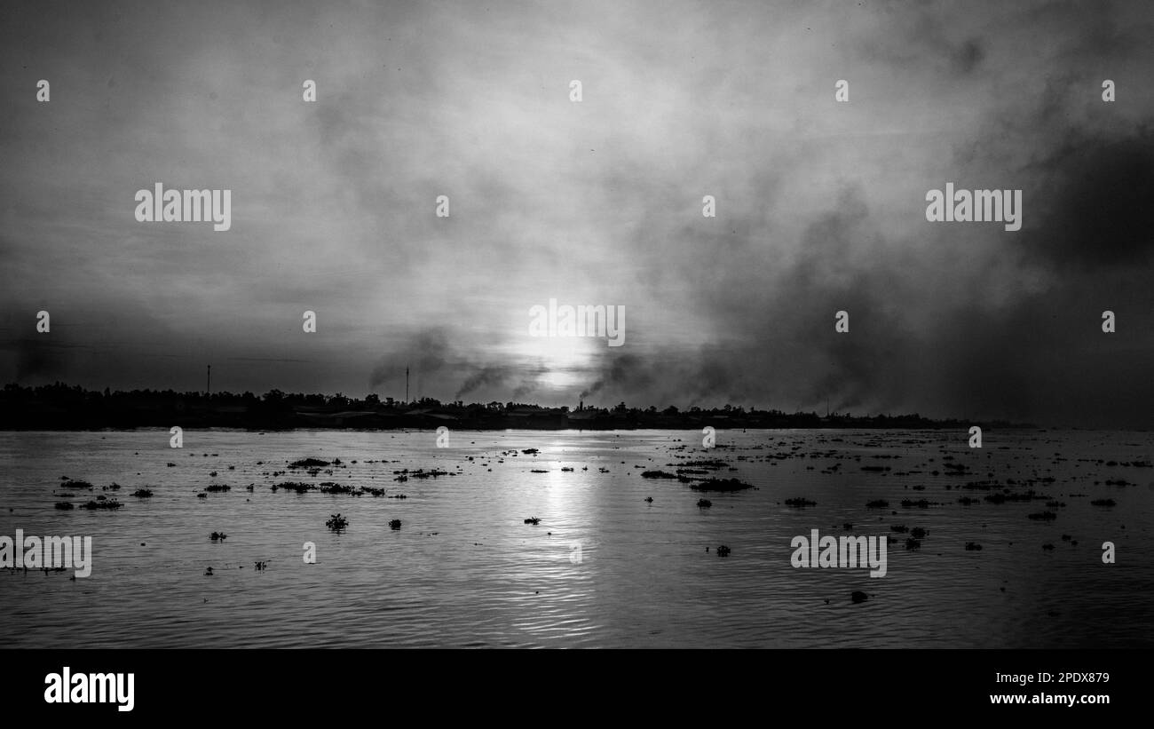 Rauchen aus Ziegelöfen, während die Sonne über dem Mekong-Fluss aufgeht, mit seinen Klumpen schwimmender Wasserhyazinthen am Long Xuyen im Mekong-Delta in Stockfoto