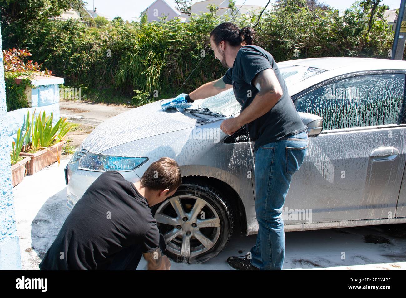 Zwei Masern reinigen einen silbernen Auto-Sprühschaum mit einem Hochdruckreiniger ein Auto waschen Stockfoto