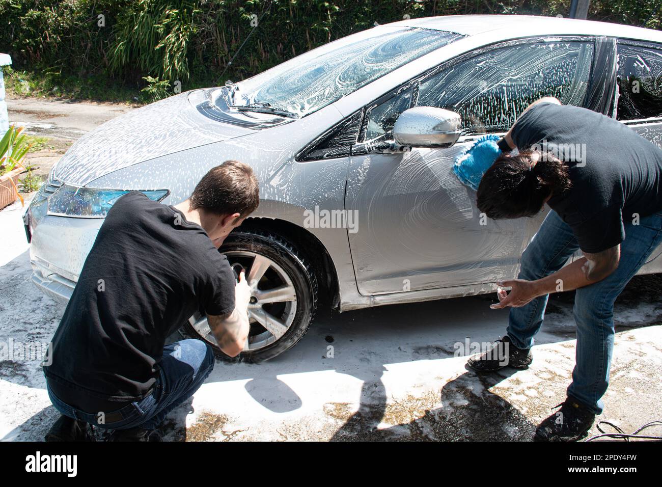 Zwei Masern reinigen einen silbernen Auto-Sprühschaum mit einem Hochdruckreiniger ein Auto waschen Stockfoto