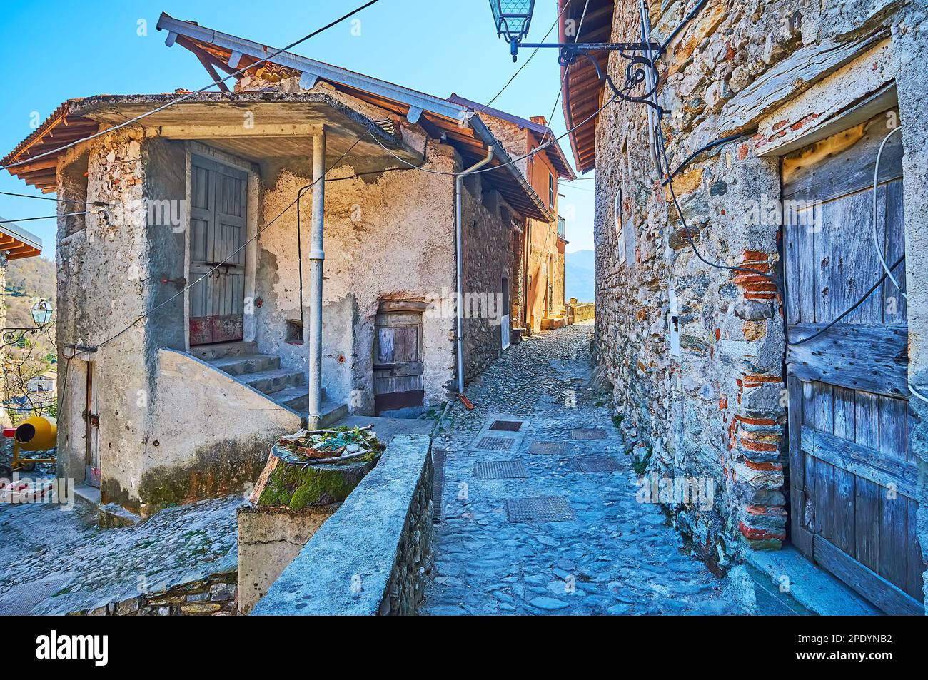 Die schmale, geschwungene Straße, gesäumt von alten schäbigen Steinhäusern, Castello, Valsolda, Italien Stockfoto