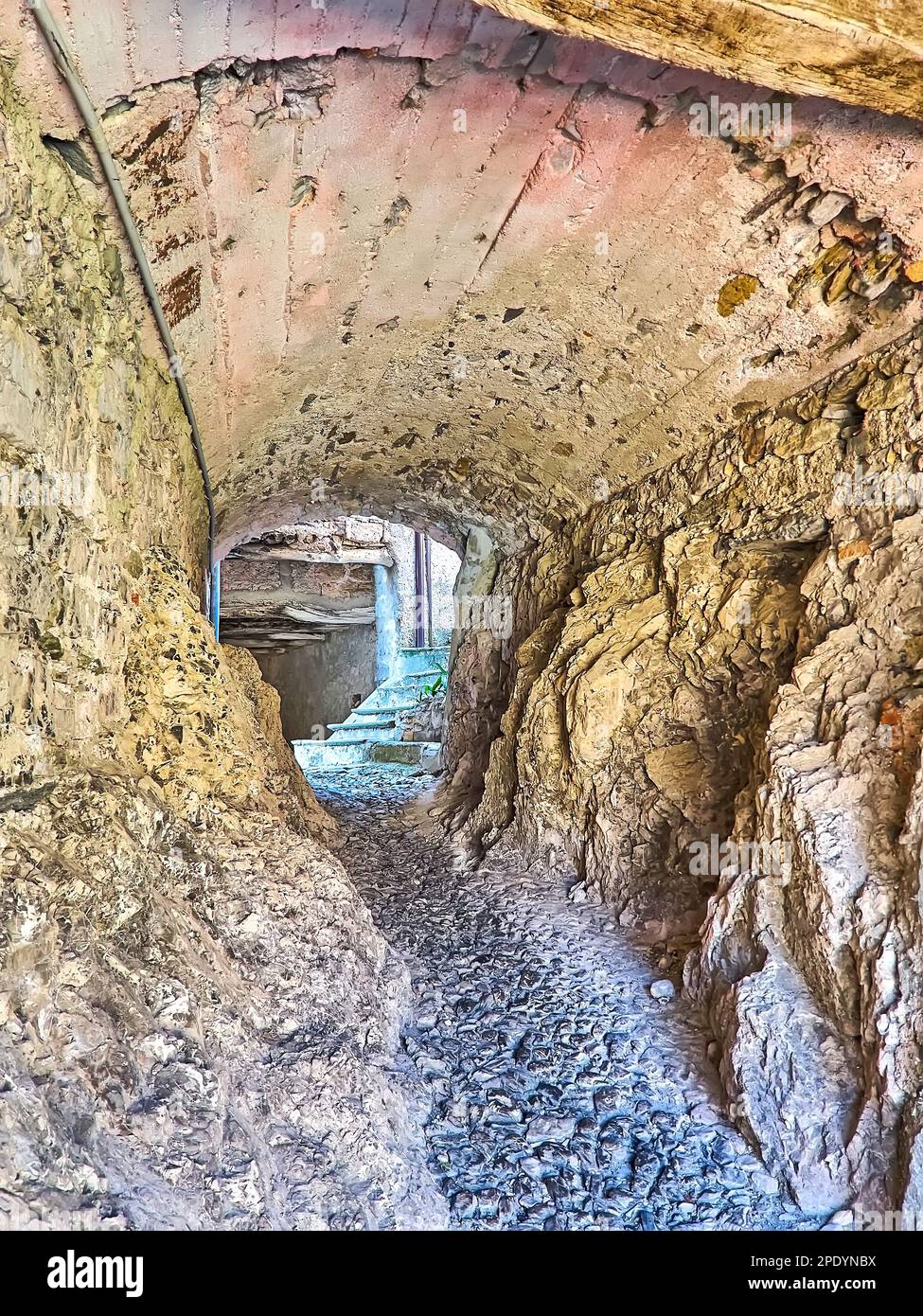 Die enge Gasse unter dem Haus mit rauen Felswänden und Betongewölbe, Castello, Valsolda, Italien Stockfoto