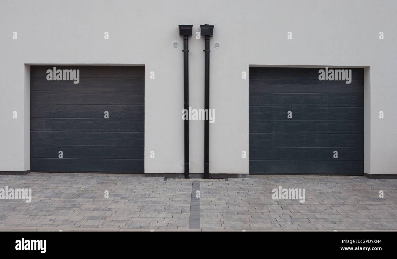 Zwei graue Rollläden in der Garage an der weißen Fassade. Abstand auf Gehwegen, Auffahrt. Stockfoto