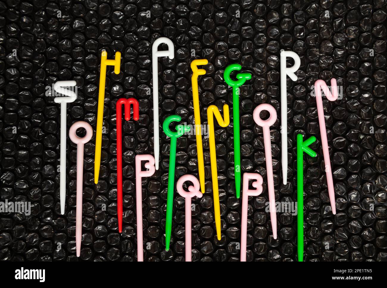 Bunte Kunststoffstäbe mit englischen Buchstaben auf der Oberseite, die auf Schwarz gestreut sind. Lustiges pädagogisches Spielzeug für Kinder, die das Alphabet lernen Stockfoto