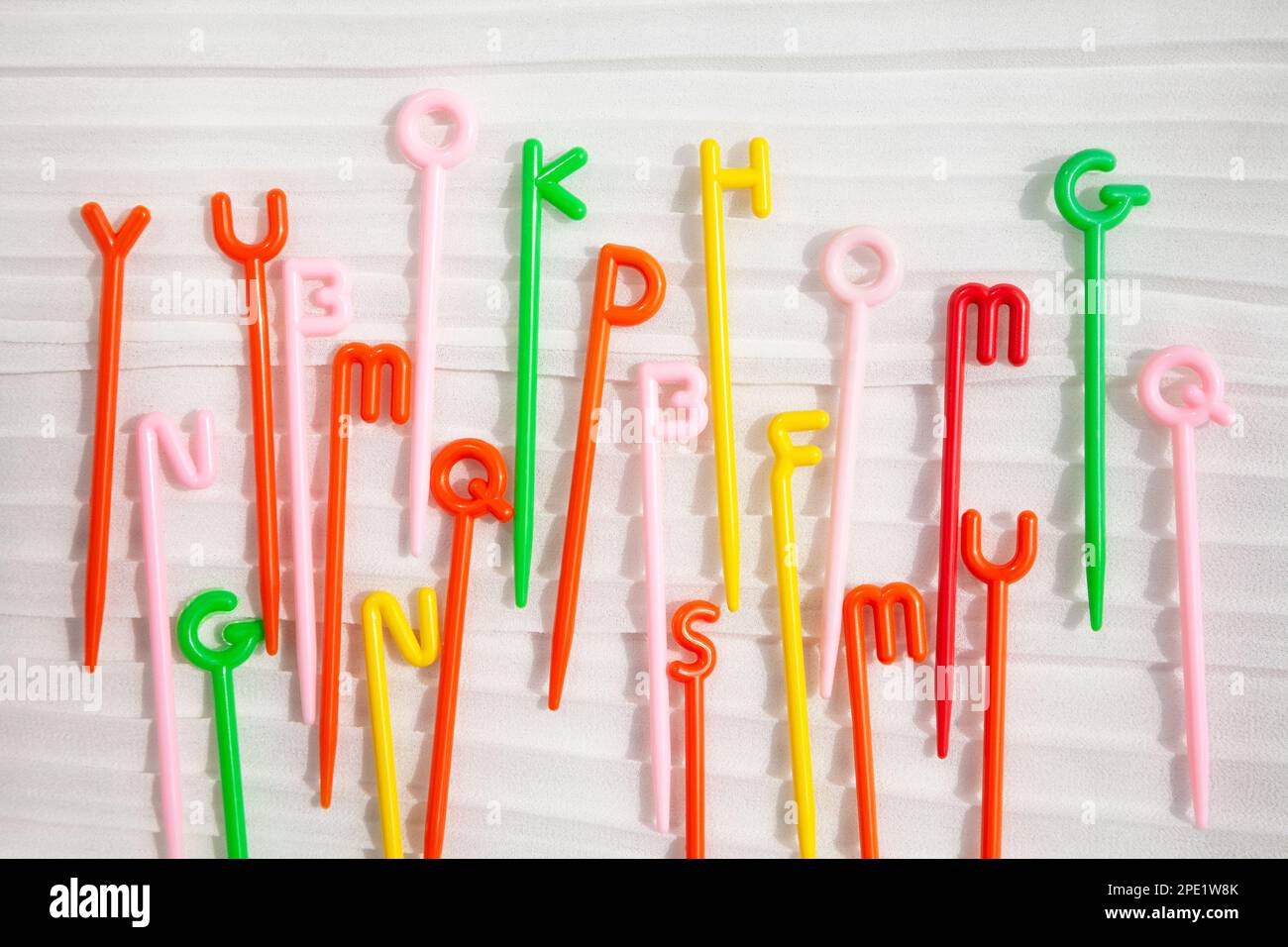 Bunte Kunststoffstäbe mit englischen Buchstaben auf der Oberseite, die auf Weiß gestreut sind. Lustiges pädagogisches Spielzeug für Kinder, die das Alphabet lernen Stockfoto