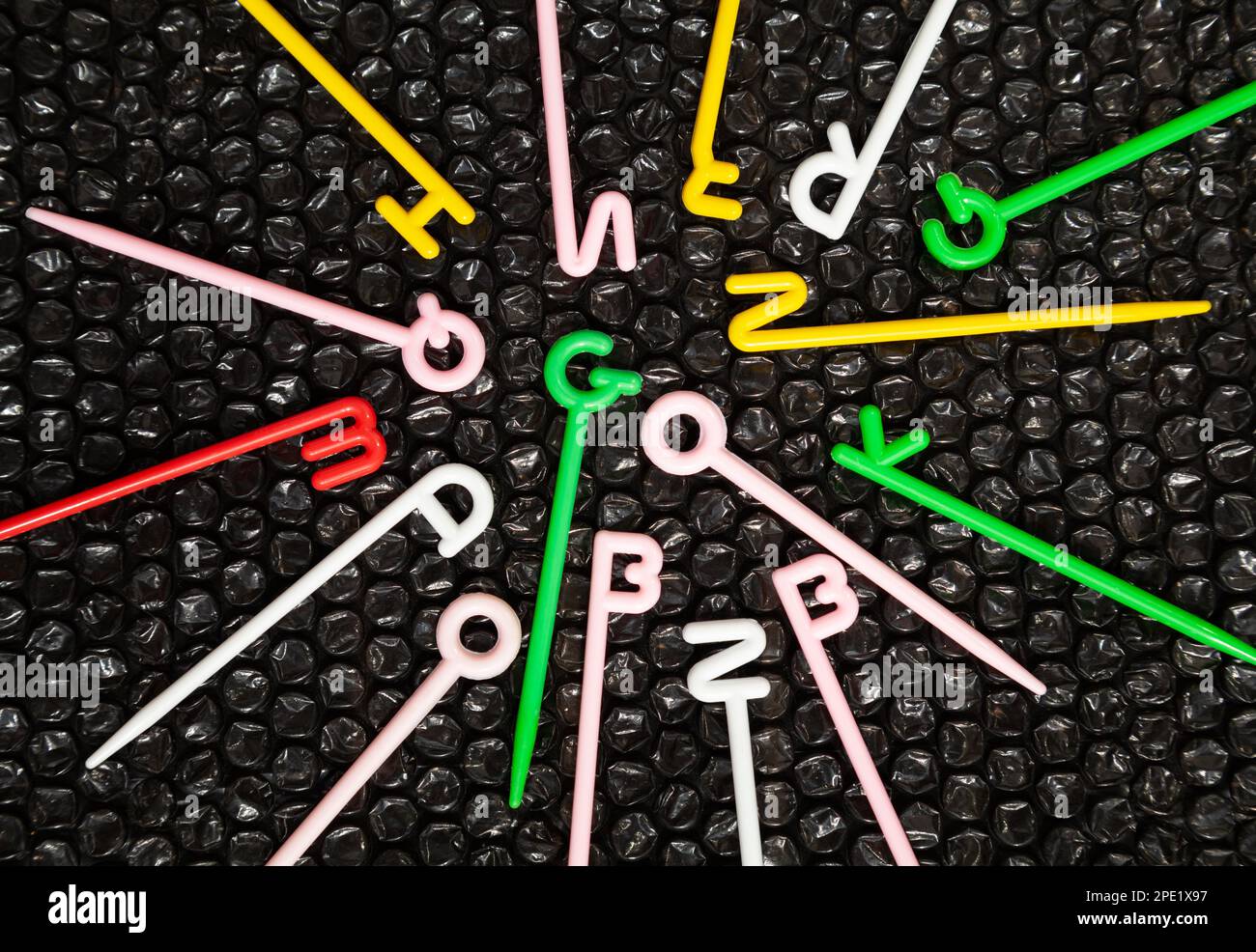 Bunte Kunststoffstäbe mit englischen Buchstaben auf der Oberseite, die auf Schwarz gestreut sind. Das Wort geht in die Mitte. Lustiges pädagogisches Spielzeug für Kinder, die das Alphabet lernen Stockfoto
