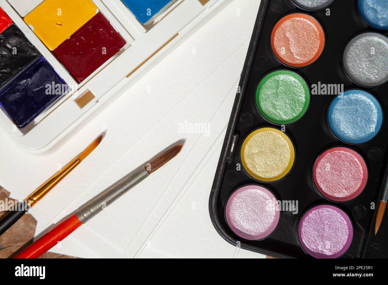 Kunstbedarf Nahaufnahme: Normale und schimmernde Aquarellfarben, Pinsel, Papier. 2 Sets Aquarellen für einen Künstler Stockfoto