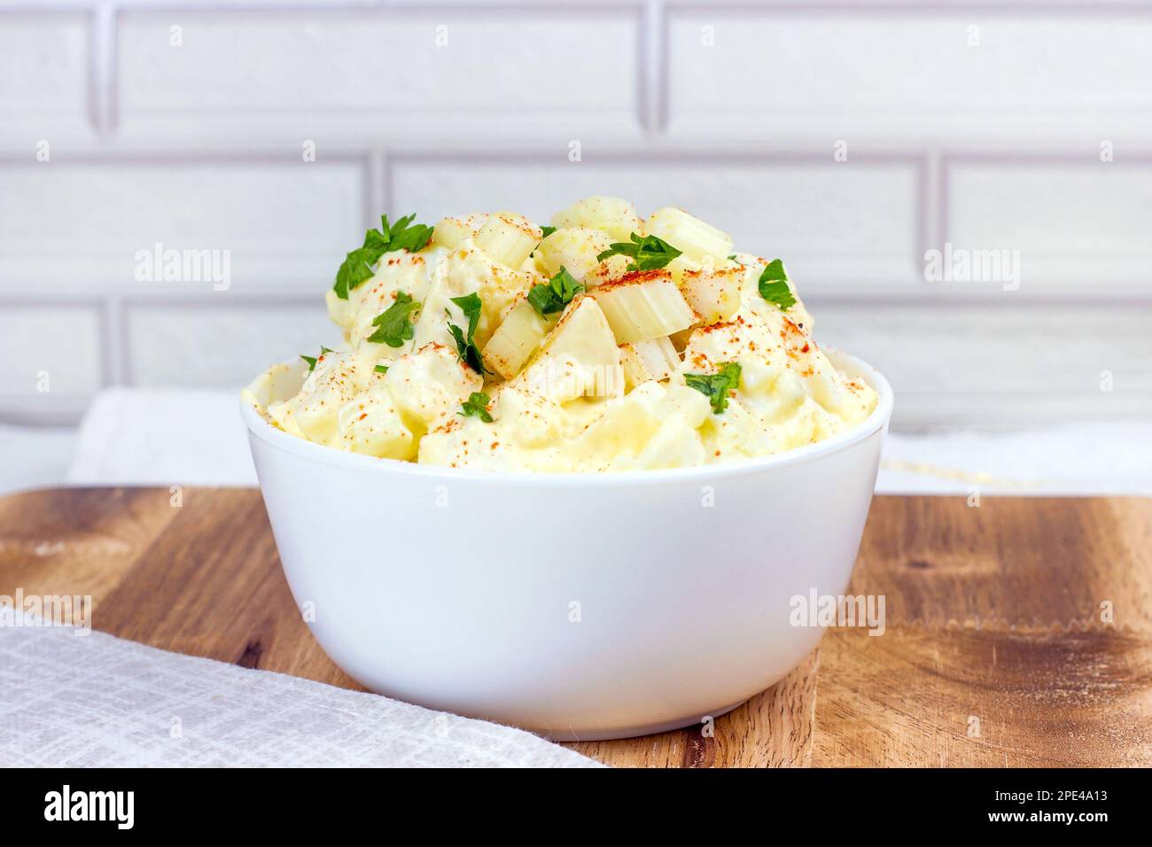 Frischer, hausgemachter traditioneller Amish-Kartoffelsalat mit Kartoffeln, gekochten Eiern, cremigem Dressing und Sellerie in einer weißen Schüssel auf Holzhintergrund Stockfoto