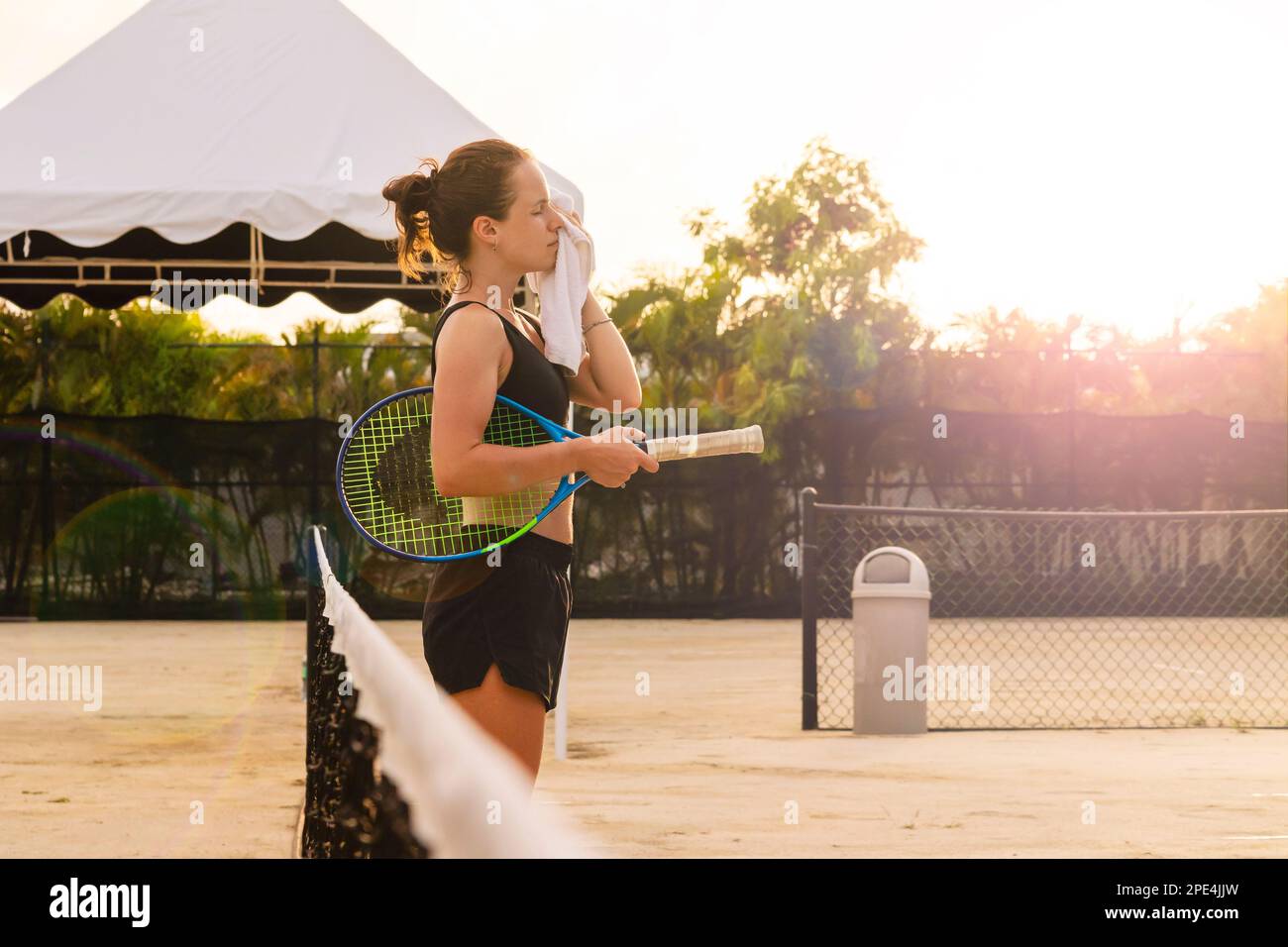 Tennisspielerin, die sich das Gesicht mit einem Handtuch abwischte, während sie auf dem Tennisplatz stand. Stockfoto