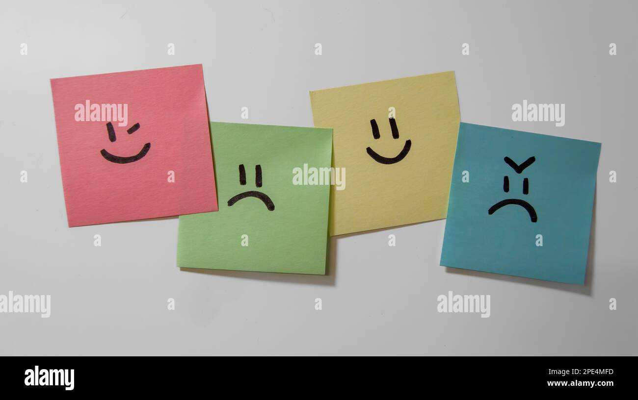 Aufklebernotizen auf weißem Hintergrund. Haftnotizen mit Smiley-Gesichtern. Blinzeln, traurig, glücklich und wütend. Stockfoto