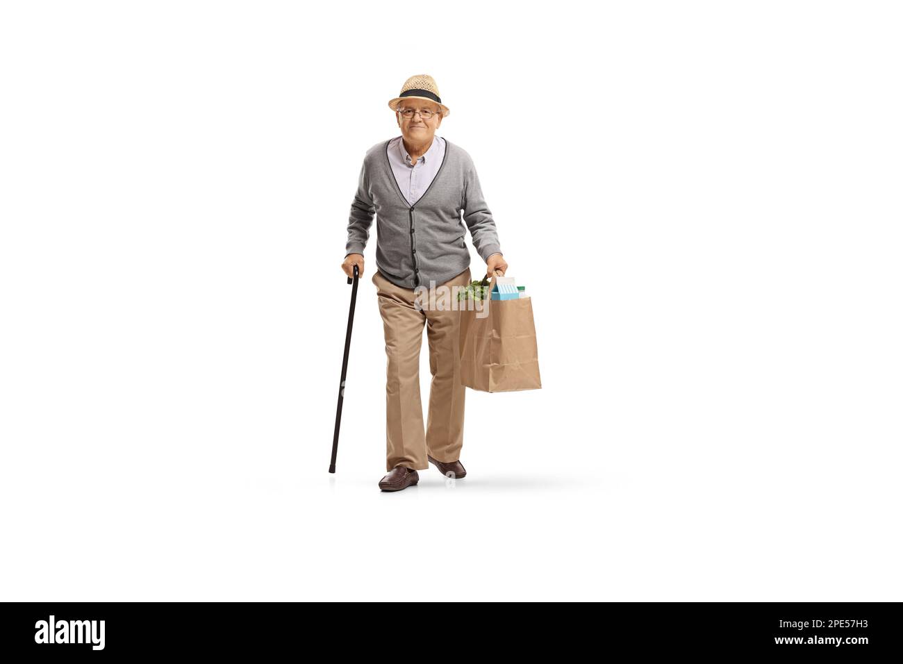 Das Gesamtbild eines älteren Mannes mit einem Gehstock, der eine Einkaufstasche aus Papier trägt, isoliert auf weißem Hintergrund Stockfoto
