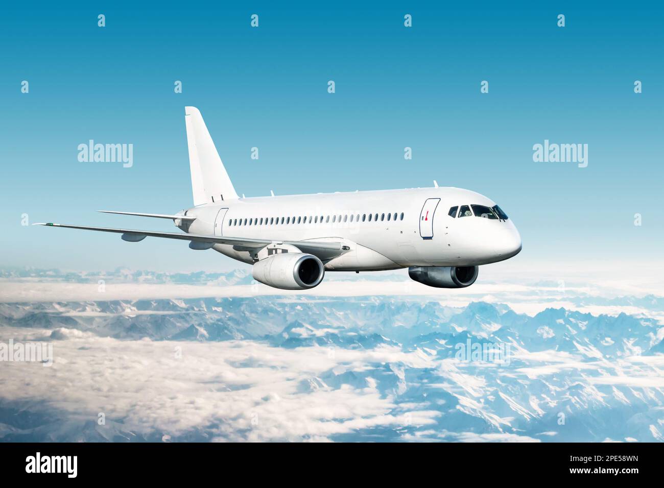 Das weiße, moderne Düsenflugzeug fliegt über schneebedeckte Bergketten Stockfoto