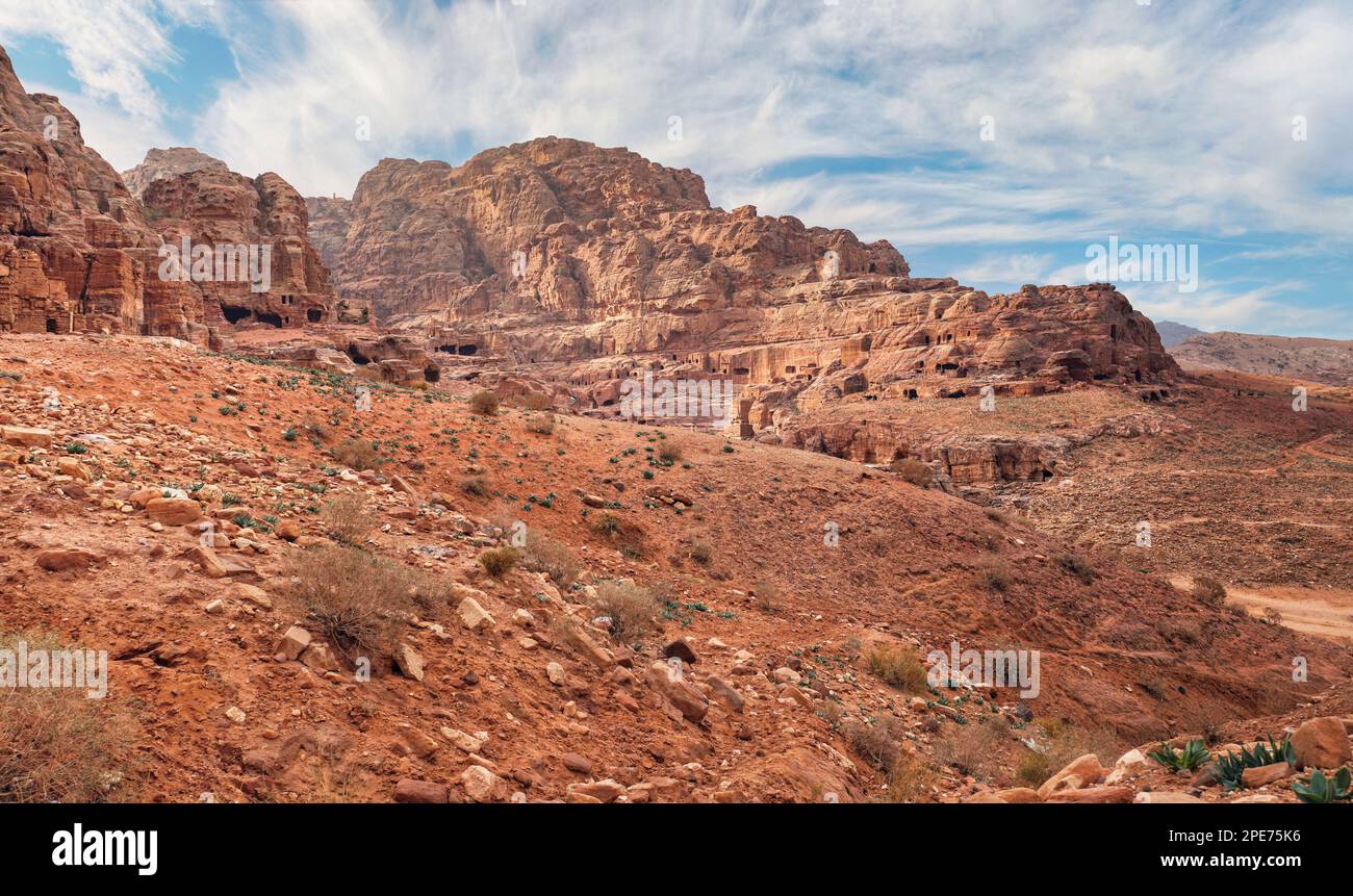 Typische Landschaft bei Petra, Jordanien, roter staubiger Boden, Berge mit geschnitzten Gebäuden in der Ferne Stockfoto