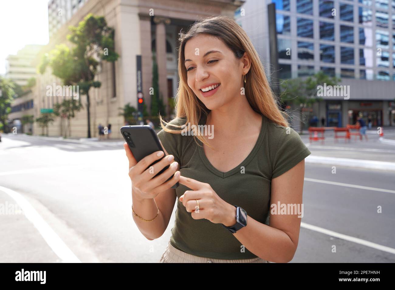 Eine schöne lächelnde Frau, die in einer modernen Metropole gute Nachrichten auf dem Smartphone erhält Stockfoto