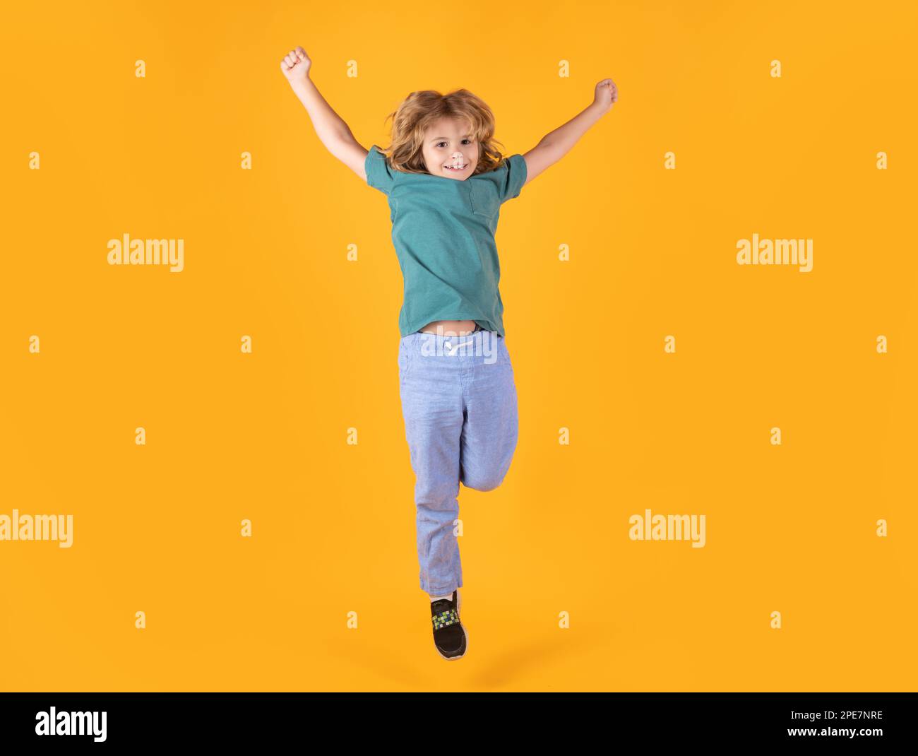 Ein energiegeladener Junge springt und hebt die Hände auf isoliertem Studiohintergrund. Ganzkörperfoto eines Sprungkindes, der schnell einen Runni hochjagt Stockfoto