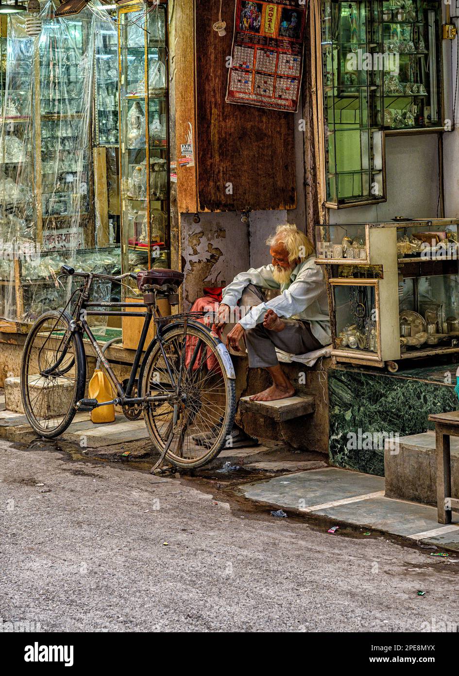 Ein alter Mann sitzt neben seinem Fahrrad in einer Seitenstraße von Chandni Chowk in Old Delhi Stockfoto