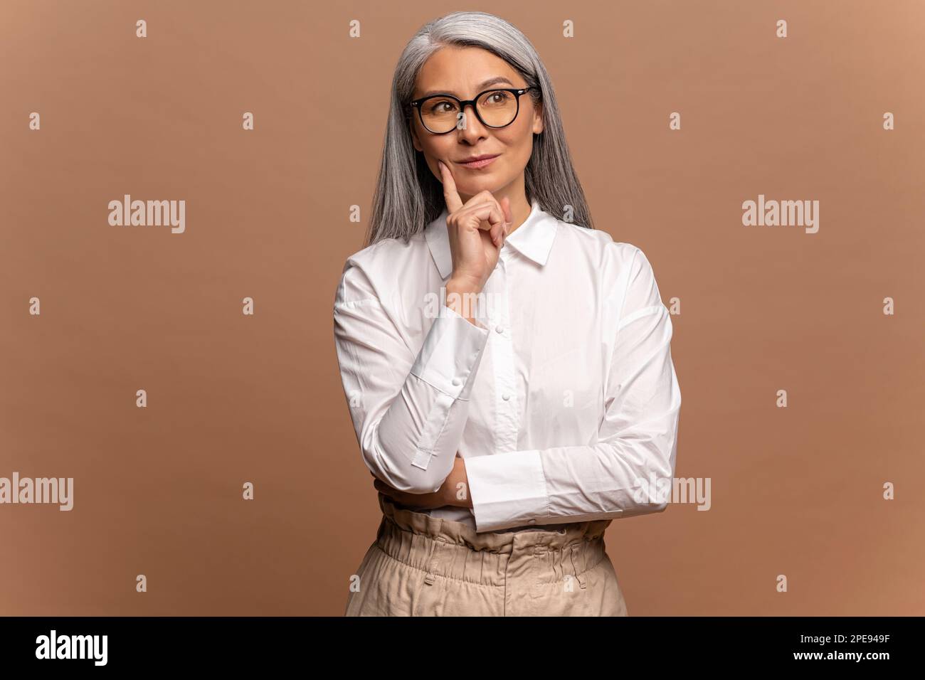 Porträt einer wohlüberlegten asiatischen Frau im weißen Hemd, die über ernste Probleme nachdenkt, mit unsicherem zögerlichen Ausdruck aussieht, eine schwierige Entscheidung trifft. Innenstudio isoliert auf beigefarbenem Hintergrund Stockfoto