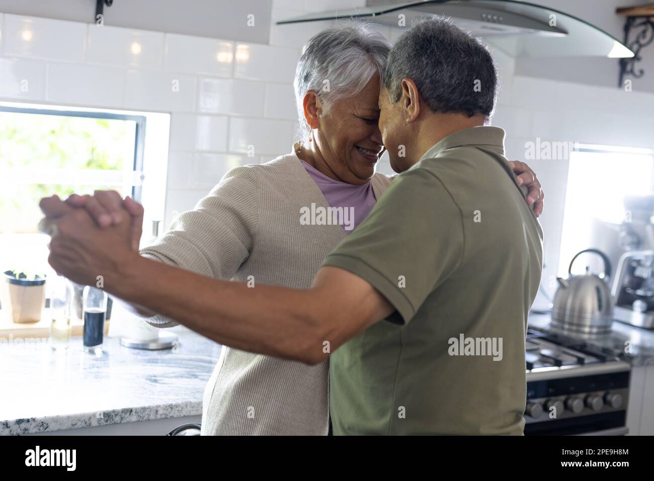 Ein birassisches Seniorenpaar mit Kopf an Kopf, Händchen halten und in der Küche tanzen. Kopierraum, unverändert, Liebe, zusammen, Ruhestand, Romantik, genießt ein Stockfoto