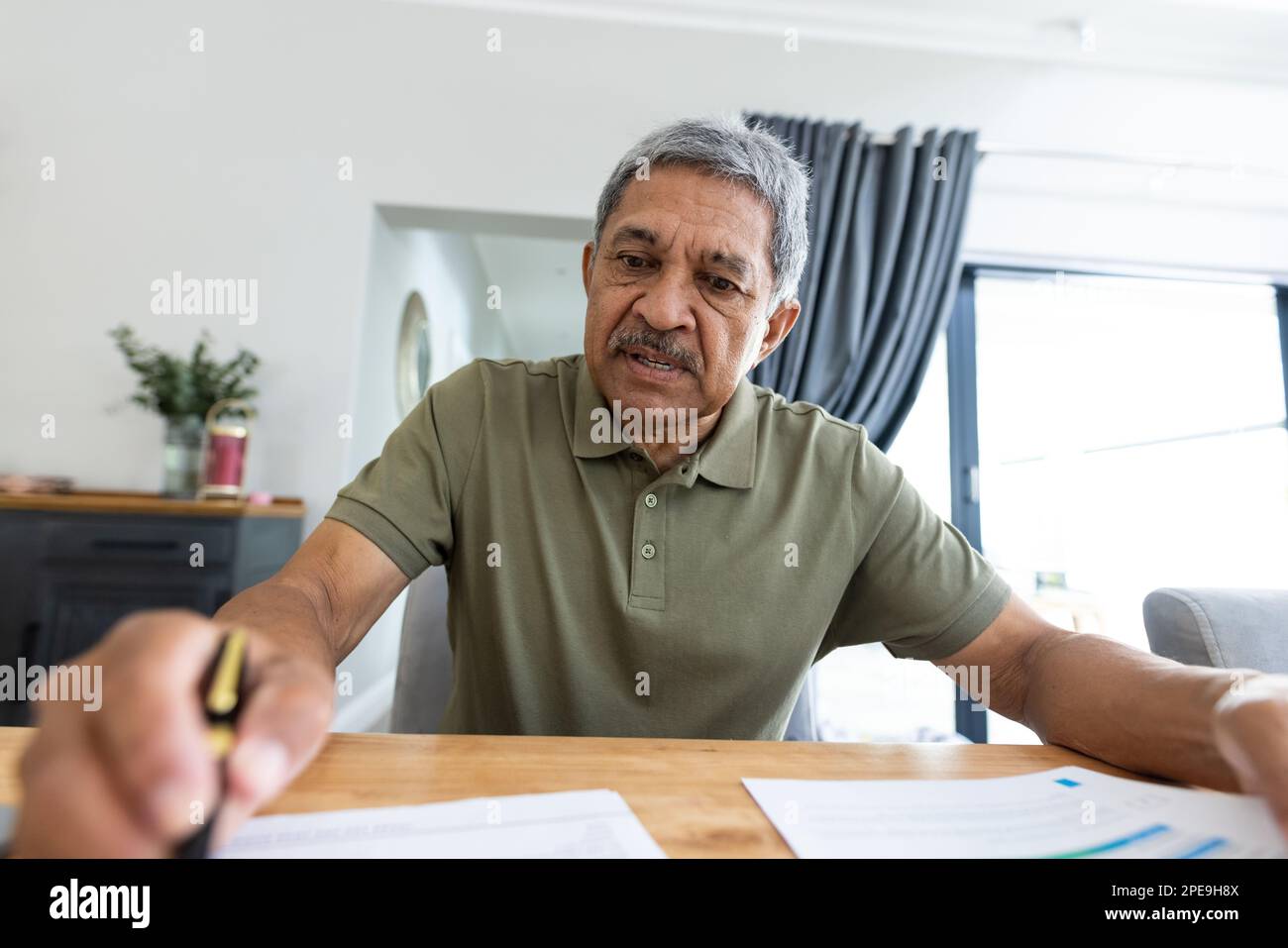 Fokussierter, birassistischer Senior-Mann, der Rechnungen auf einem Holztisch analysiert, während er zu Hause sitzt. Kopierraum, unverändert, Lifestyle, Haushaltsfinanzierung, Budget und Ruhestand Stockfoto