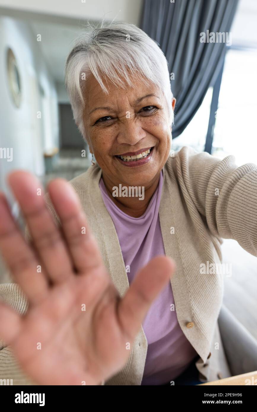 Nahaufnahme eines fröhlichen, birassistischen Seniorenfrauen, die zu Hause mit der Hand winken, während sie bei einem Videogespräch miteinander reden. Unveränderter Lebensstil, glücklich, Geste, Kommunikation Stockfoto