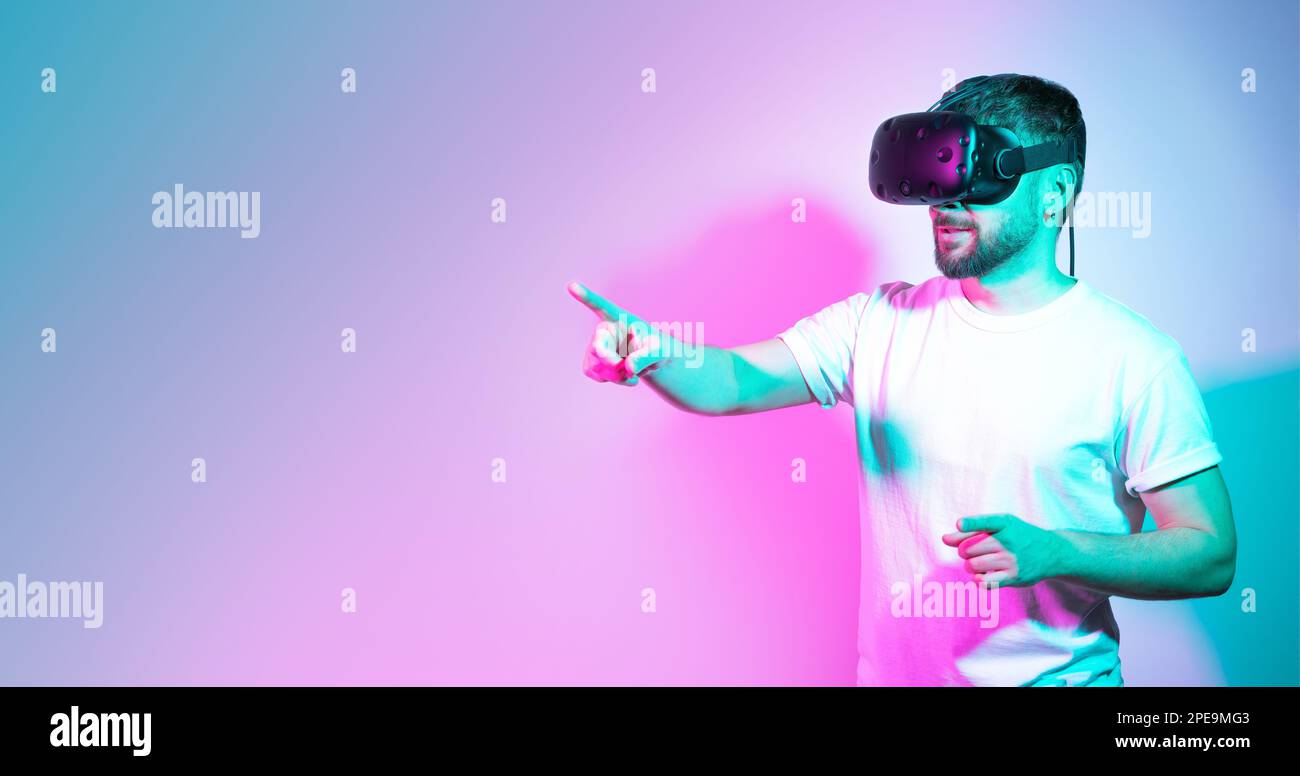 Ein bärtiger Mann mit Brille spielt und versucht, etwas im farblich abgestuften Neonhintergrund zu berühren. Augmented-Reality-Technologie, Online-Spiel, Unterhaltung Stockfoto