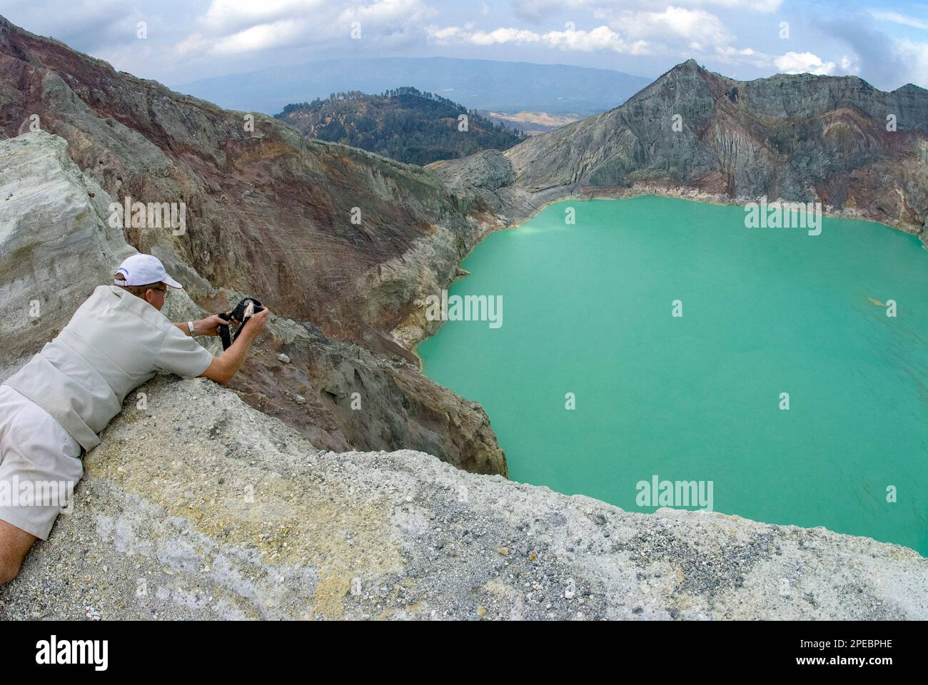 Man (Modell veröffentlicht) am Rand mit Blick auf den türkisgrünen See und die Seite des Kraters, Mount Ijen, Ost-Java, Indonesien Stockfoto