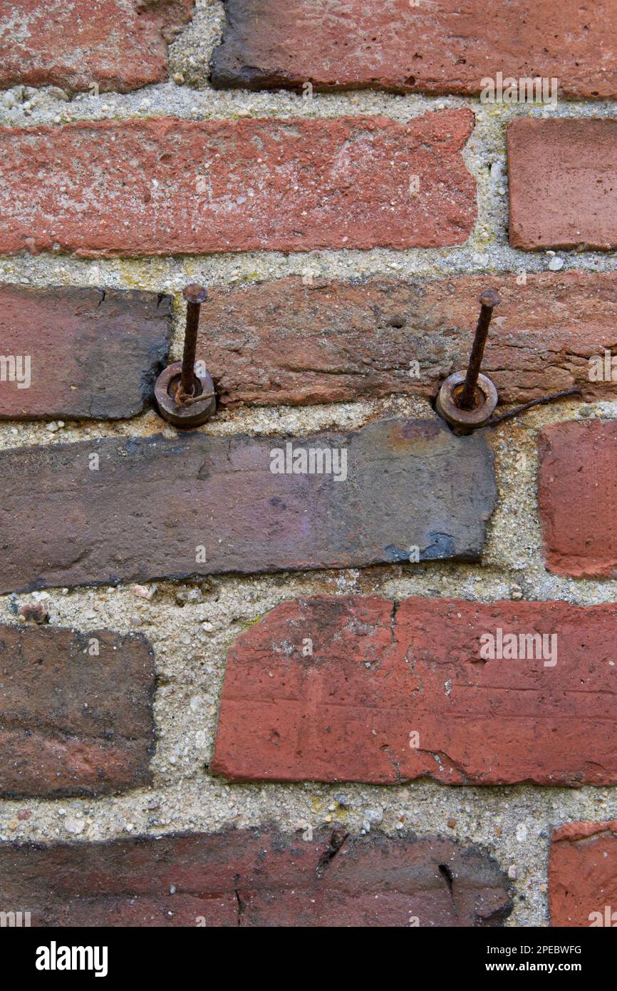 Zwei (2) rostige Nägel an alten roten Ziegelwänden. Texturierter Hintergrund aus Mauerwerk auf altem Gebäude. Ziegel sind ungleichmäßig verlegt. Stockfoto