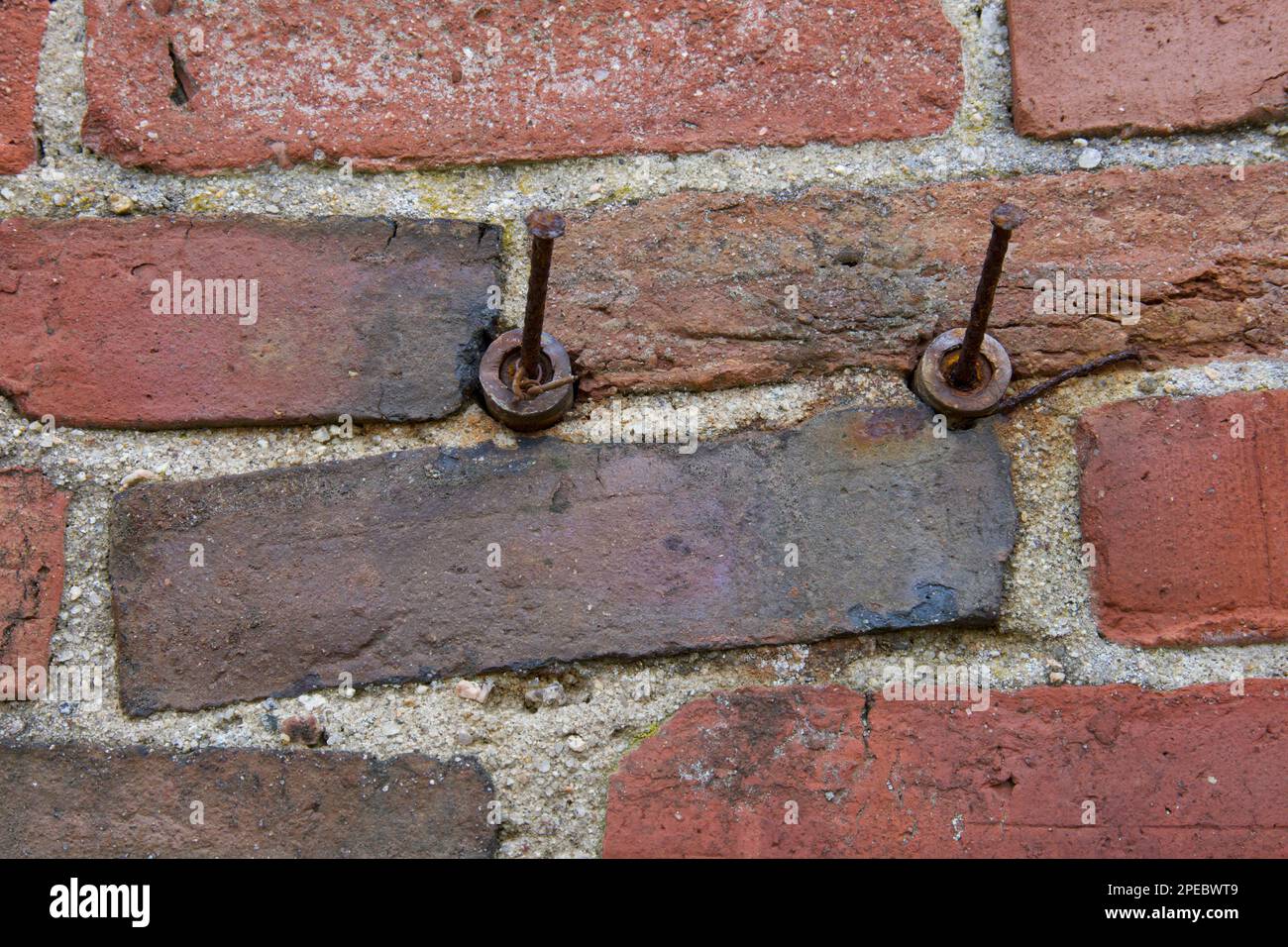 Zwei (2) rostige Nägel an alten roten Ziegelwänden. Texturierter Hintergrund aus Mauerwerk auf altem Gebäude. Ziegel sind ungleichmäßig verlegt. Stockfoto