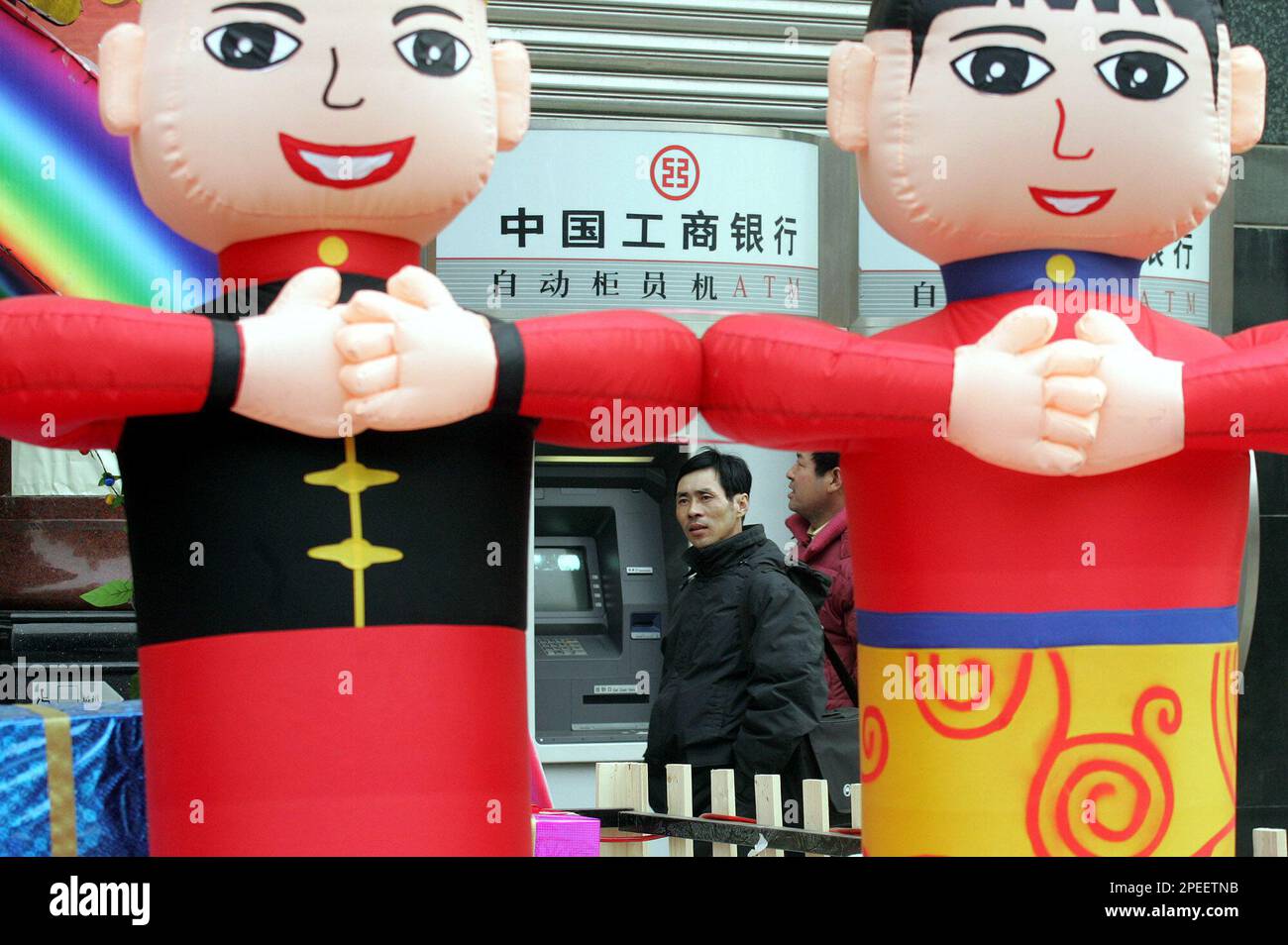 A Chinese man walks past inflatable Chinese dolls near an ATM machine for the Industrial and Commercial Bank of China in Beijing Tuesday, Jan 25, 2005. An avalanche of scandals involving hundreds of millions of dollars have been uncovered at China's state-owned commercial banks, which are under scrutiny as they prepare to sell their first shares on foreign stock exchanges. (AP Photo/Ng Han Guan) Stockfoto