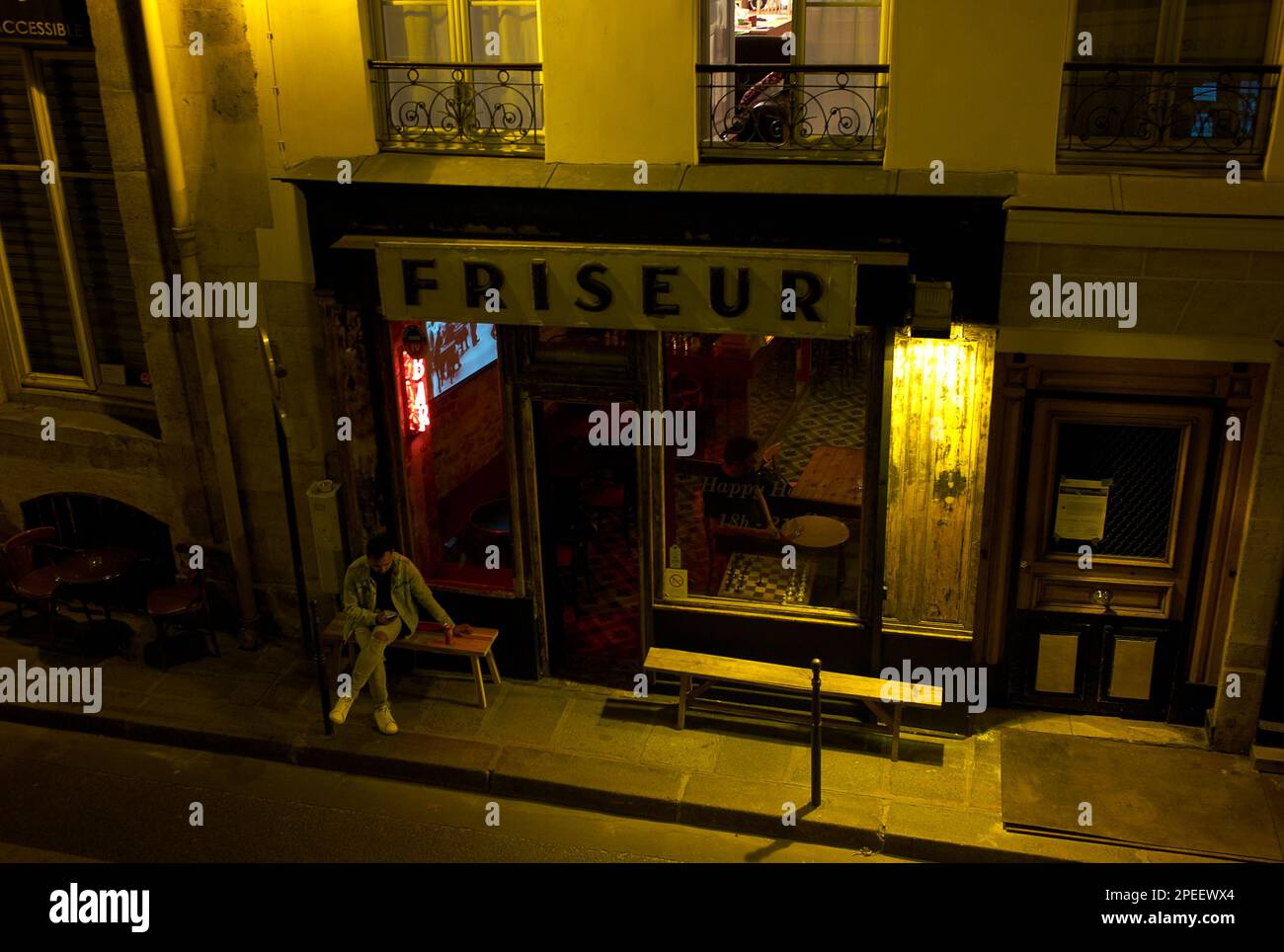 Farbfoto eines Mannes, der nachts vor der Friseur Bar sitzt, The Marais (Le Marais), Paris, Frankreich, Europa, 2022. Stockfoto
