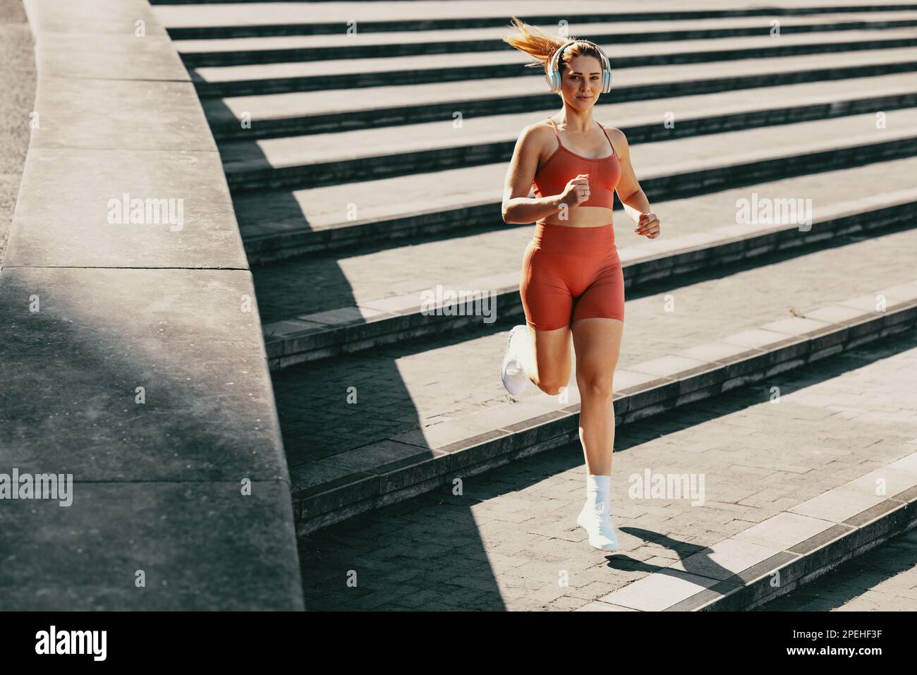 Sportlerin, die draußen mit Kopfhörern laufen will. Läuferin, die in Sportbekleidung die Treppe runterjoggt. Weibliches Training mit Herz-Kreislauf-Übungen. Stockfoto