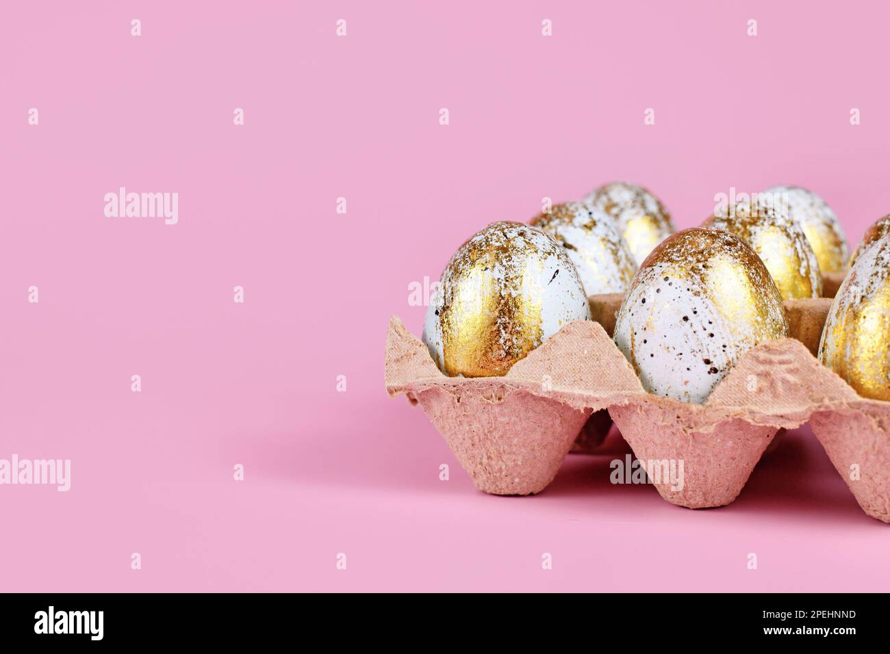 Lackierte blaue Ostereier mit goldenen Flecken im Eierkarton auf pinkfarbenem Hintergrund mit Kopierbereich Stockfoto