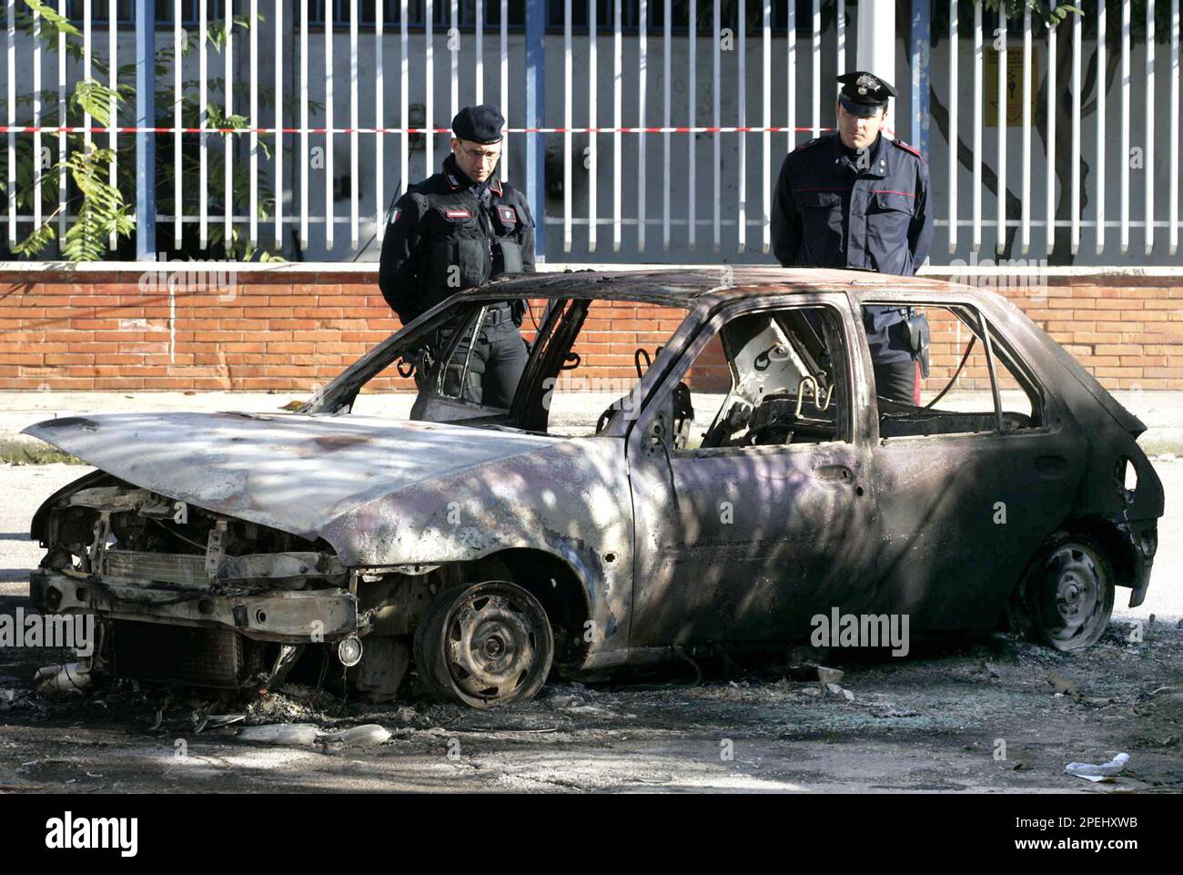 Italian carabinieri Paramilitary police officers inspect the charred car where the body of Francesco Tortora, 63, was found in Naples, Italy, Sunday, Nov. 21, 2004. Tortora was reading in his car on a quiet street near Secondigliano when two gunmen approached, fired shots, hustled the man into their car and drove off. The car was found shortly after with the man's body, burned inside. (AP Photo/Salvatore Laporta) Stockfoto