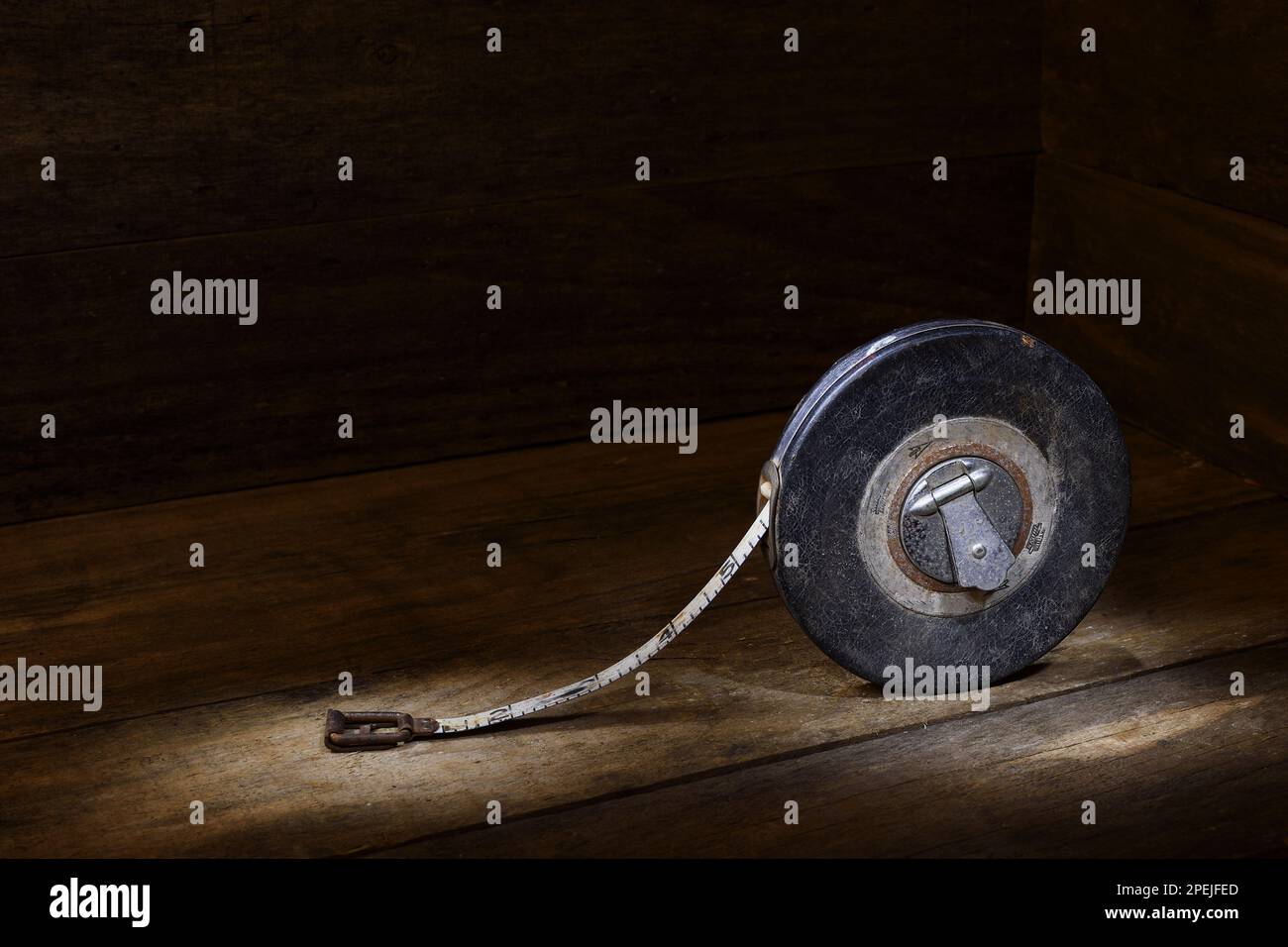 Ein schwarzes, klassisches, aufziehbares, zölliges Maßband aus Metall auf rustikalem Holz in sanfter, dunkler Stimmungsbeleuchtung, das in einem Studio aufgenommen wurde Stockfoto