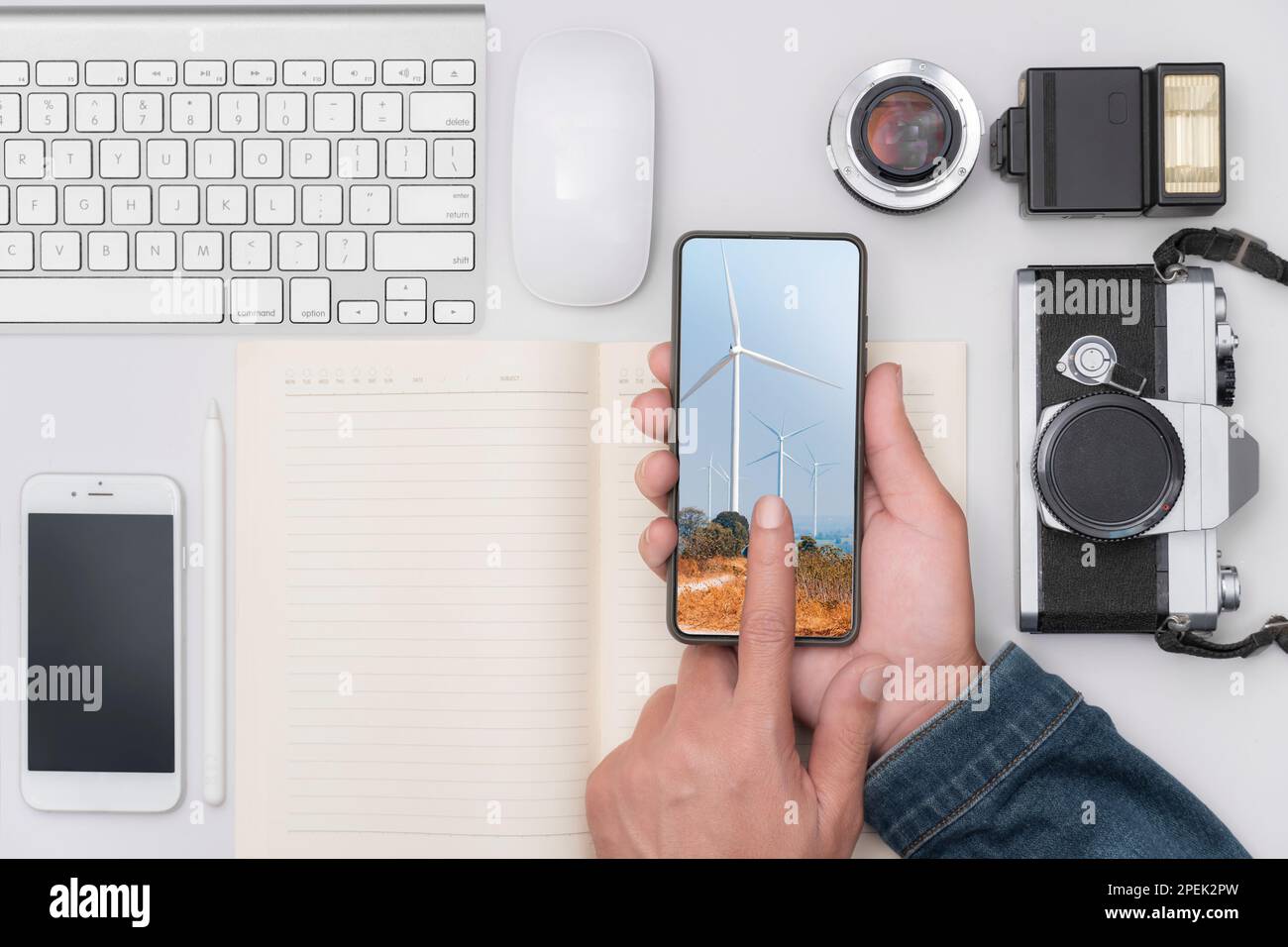 Die Hand eines Mannes hält ein Telefon auf einem Schreibtisch voller Geräte, Kameras, Telefone und Computertastaturen. Stockfoto