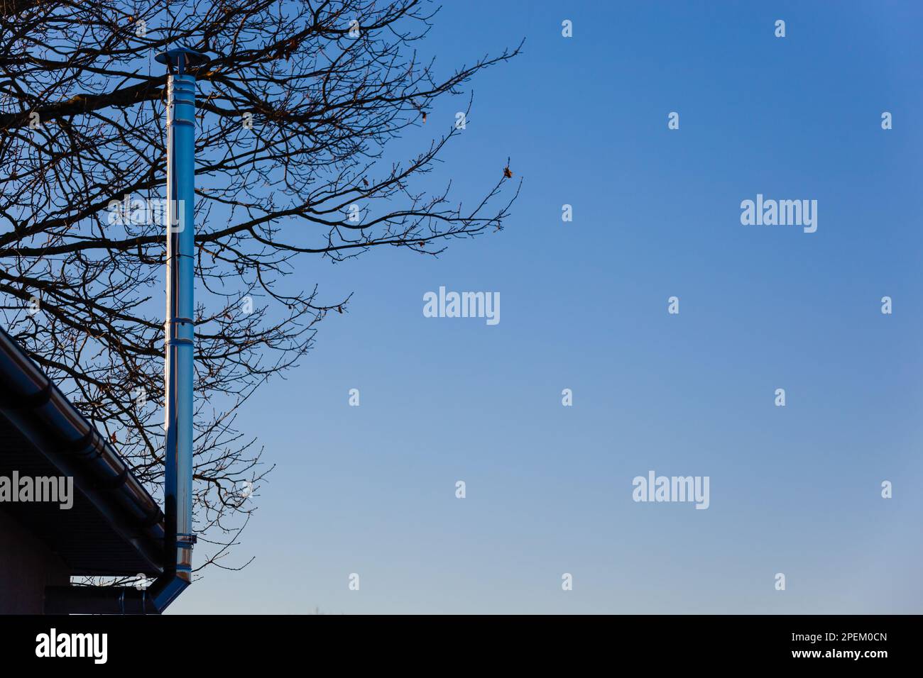 Dünner Chromschornstein auf dem Dach am blauen Himmel und Holz im Winter. Horizontal. Foto in hoher Qualität Stockfoto