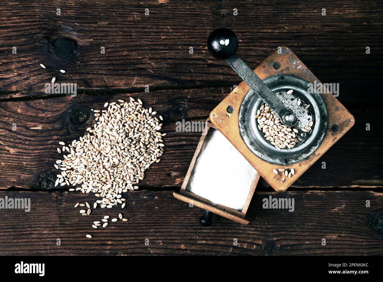 Alte Getreidemühle mit Weizenkörnern und Mehl auf rustikalem Holzhintergrund Stockfoto