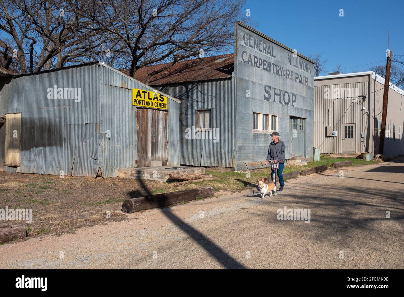 Ein älterer Mann geht mit seinem Corgi-Mischhund an der Leine eine eine Seitenstraße entlang, vorbei an Geschäften, in Mason, Mason County, Texas. Stockfoto